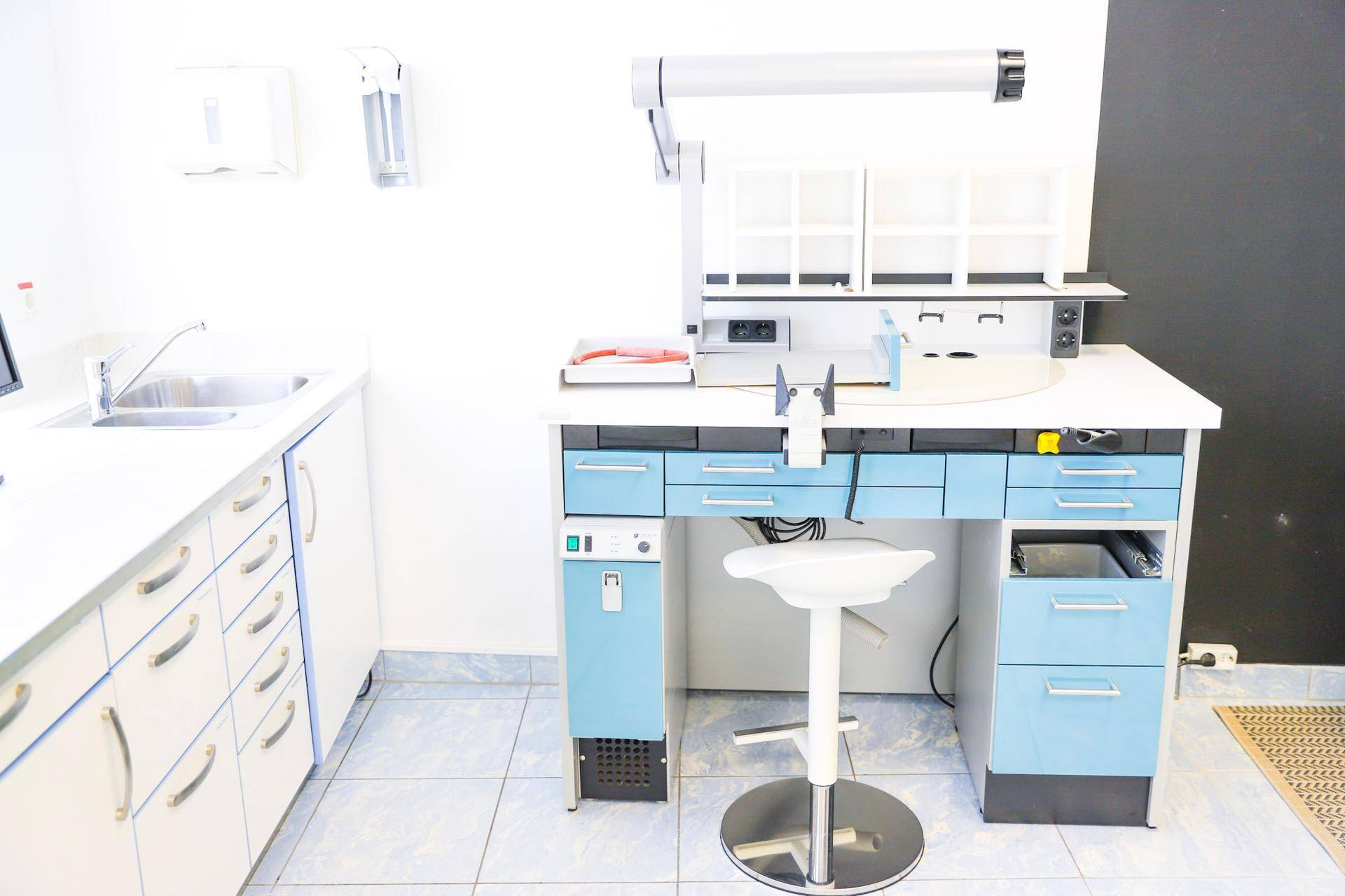 Arbeitsplatz in einem zahntechnischen Labor mit Waschbecken, blauen Schubladen und spezieller Beleuchtung.