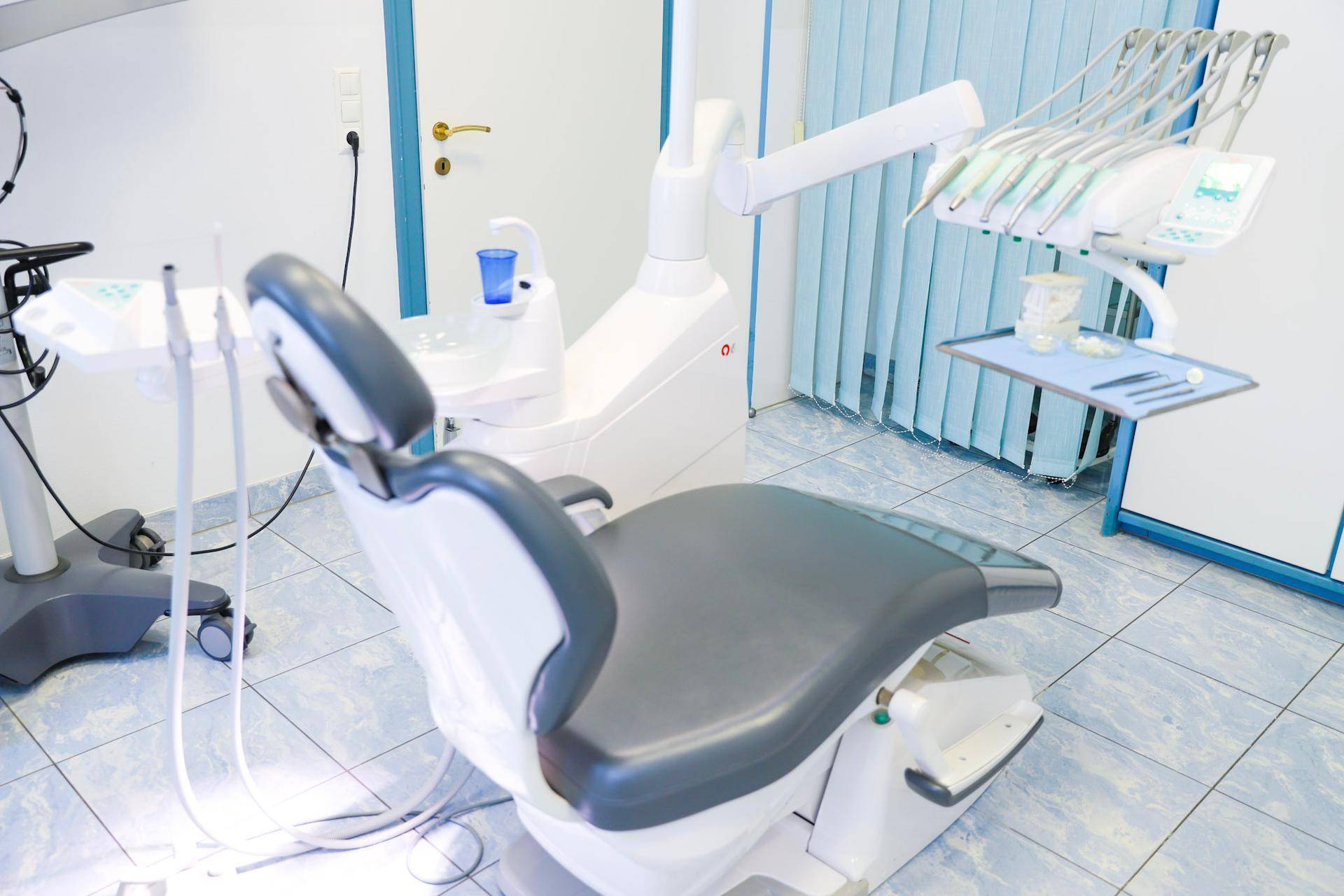 Zahnarztstuhl mit Instrumenten und blauen Vorhängen in einem sauberen und funktionalen Behandlungszimmer.