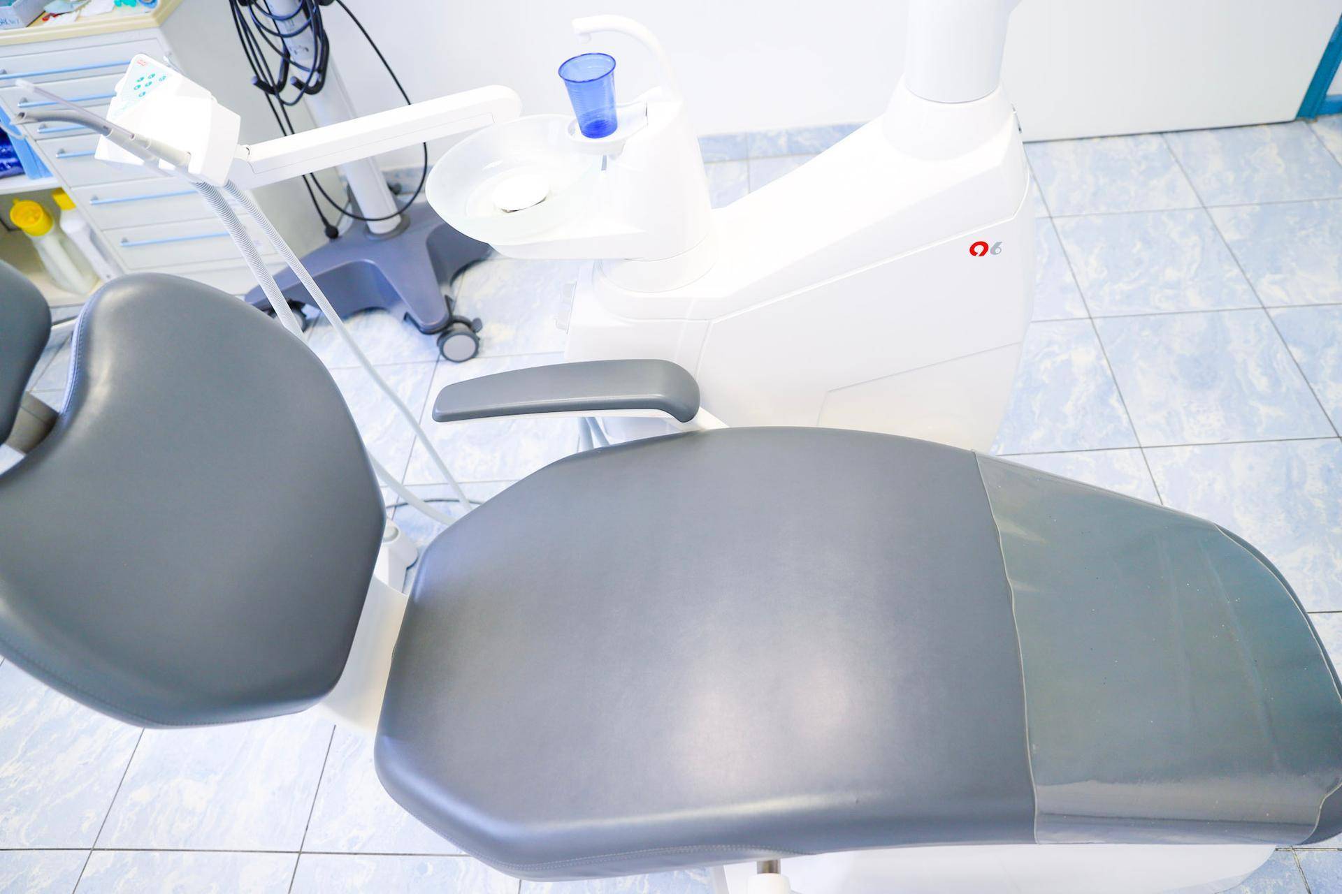 Seitenansicht eines ergonomischen Zahnarztstuhls in Grau und Weiß auf einem hellblauen Fliesenboden.