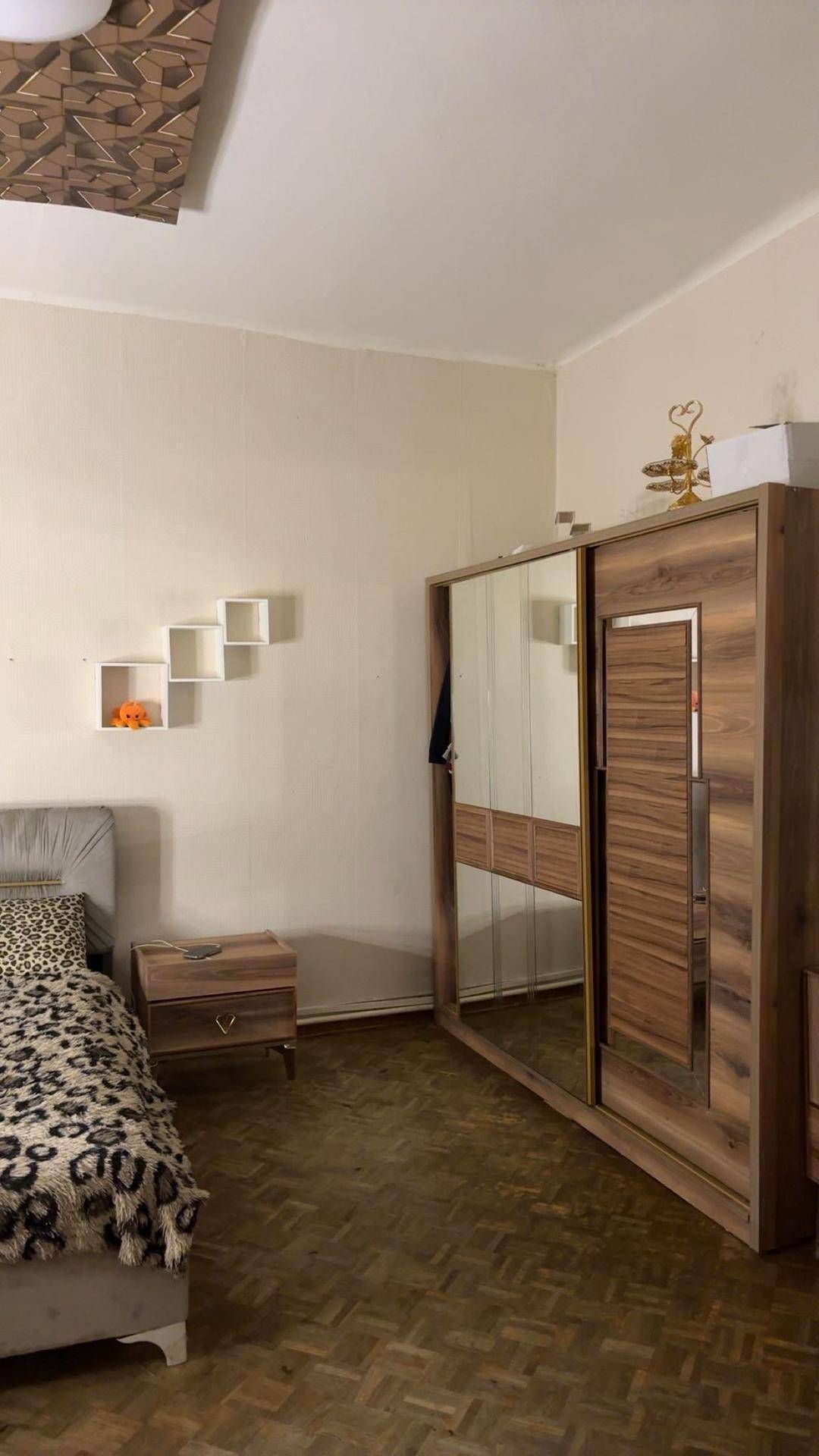 Schlafzimmer mit Doppelbett und großem Holzschrank mit Spiegeltüren auf klassischem Parkettboden.