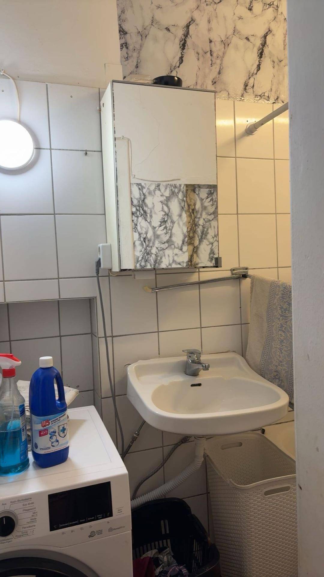 Funktionaler Waschraum mit Waschmaschine, Waschbecken und weißen Wandfliesen.