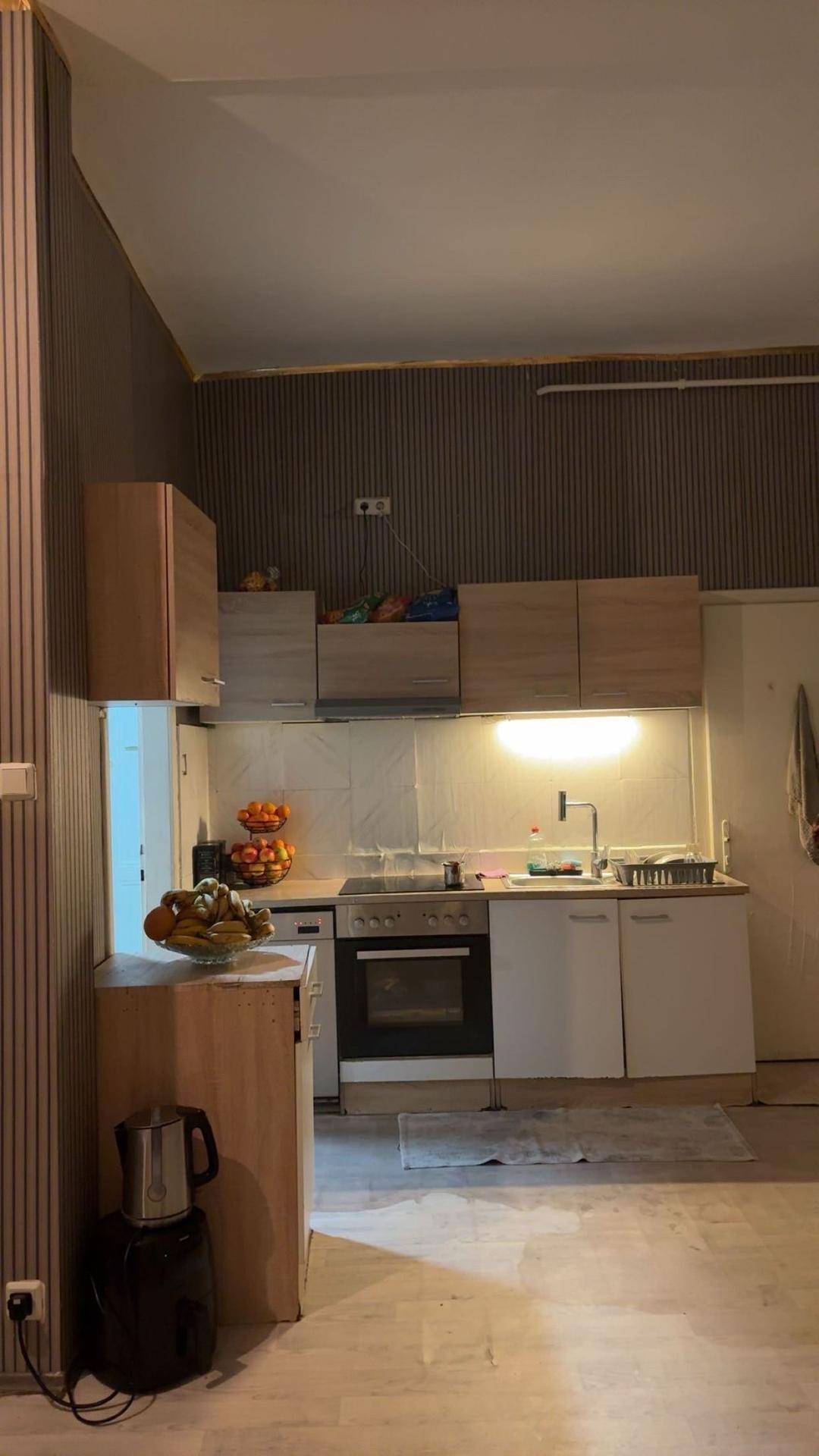 Funktionale Küche mit hellen Holzschränken, integriertem Backofen und Spülbereich unter indirekter Beleuchtung.