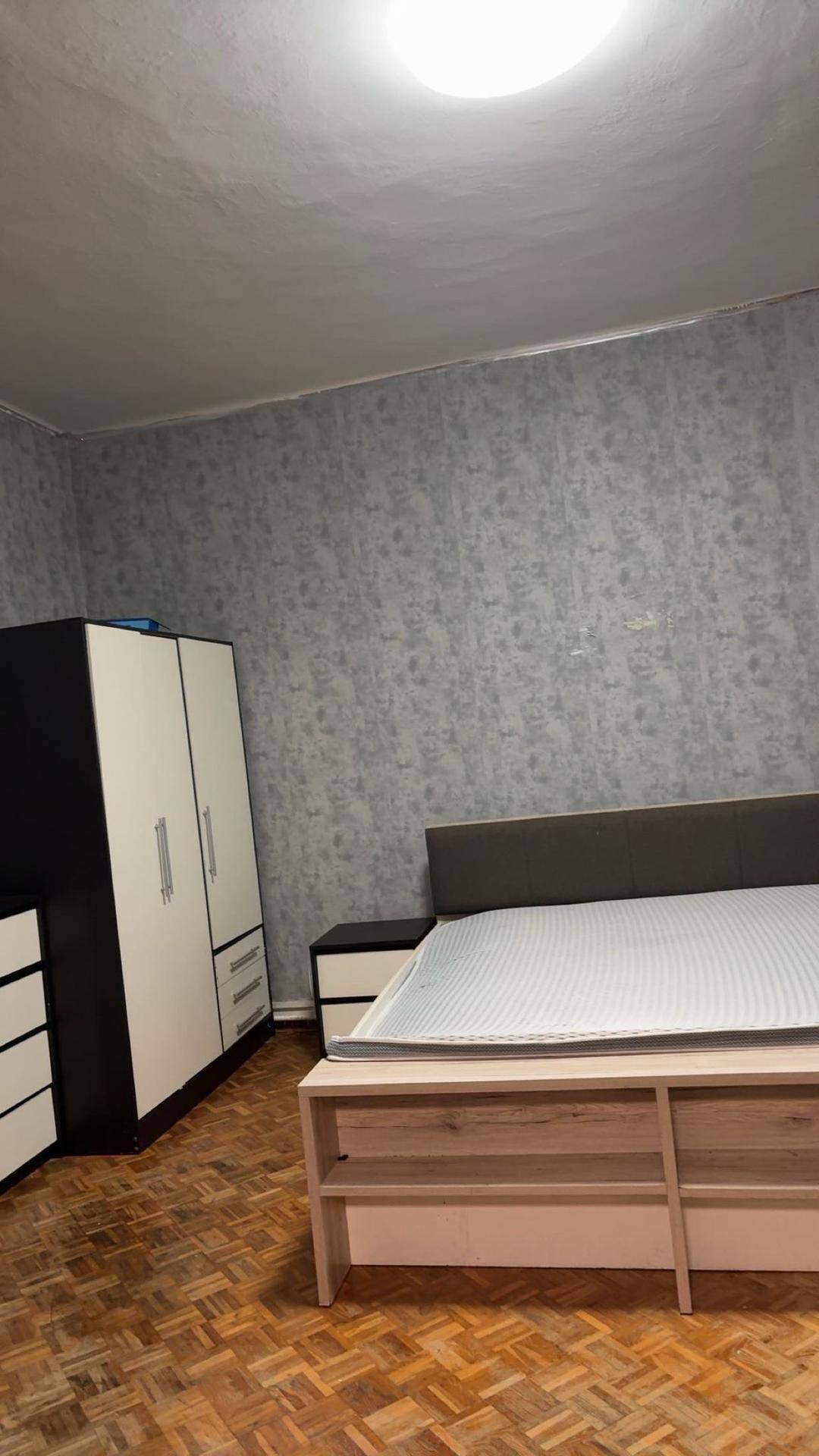 Schlafzimmer mit Doppelbett, modernem Kleiderschrank und gemusterter Tapete auf Parkettboden.