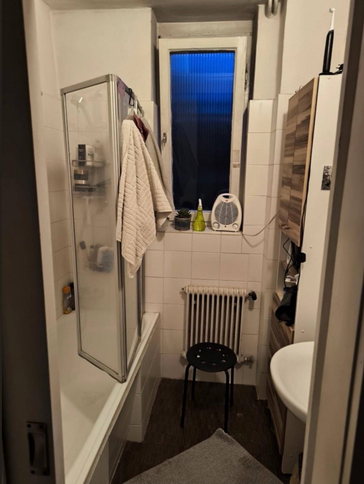 Badezimmer mit Badewanne, Duschabtrennung und Fenster, einfach gefliest und funktional.