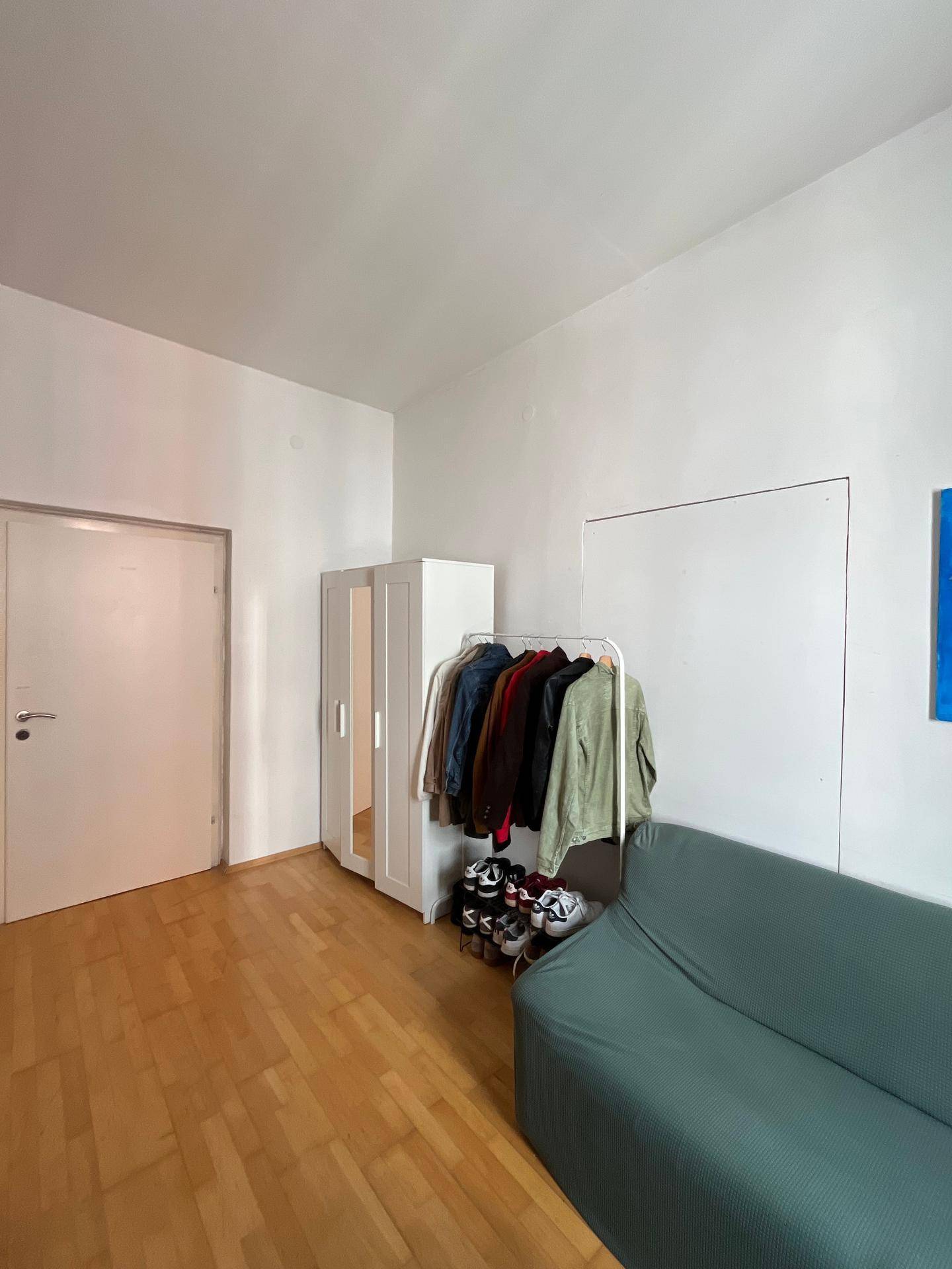 Heller Raum mit Sofa, Kleiderschrank und Holzboden, vielseitig nutzbar als Wohn- oder Schlafbereich.