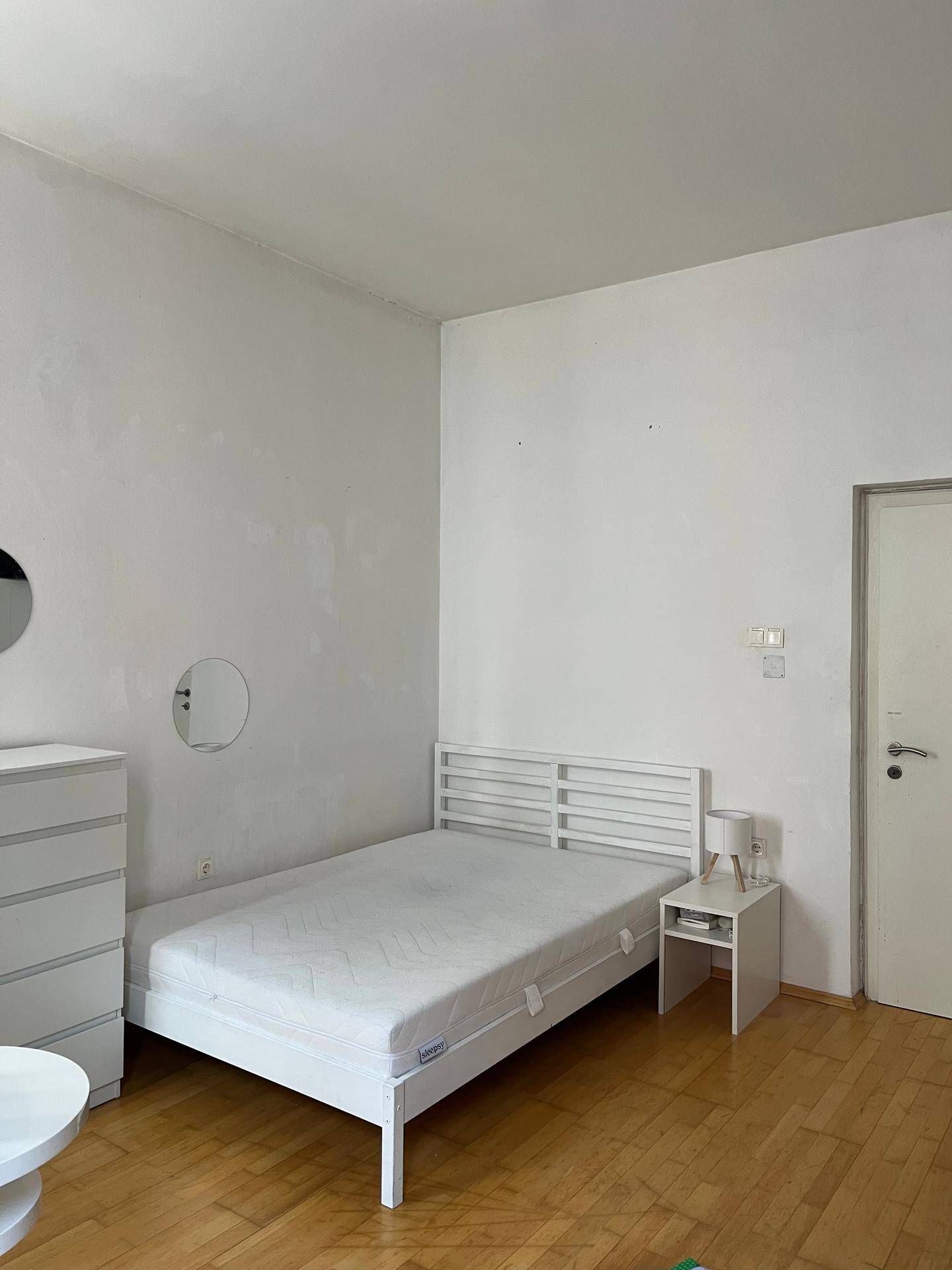 Schlafzimmer mit weißem Bett, Kommode und Holzboden, funktional und hell eingerichtet.