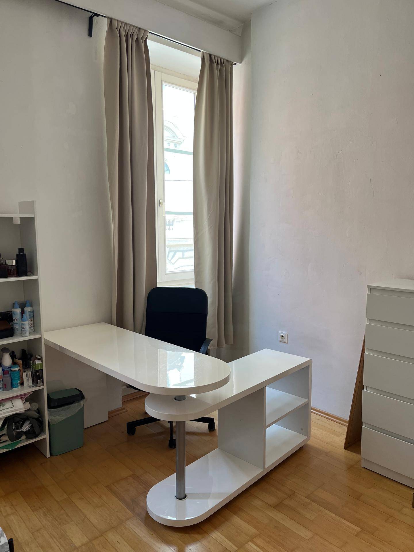 Moderner weißer Schreibtisch mit Bürostuhl in einem hellen Raum mit Holzboden und Fenster.