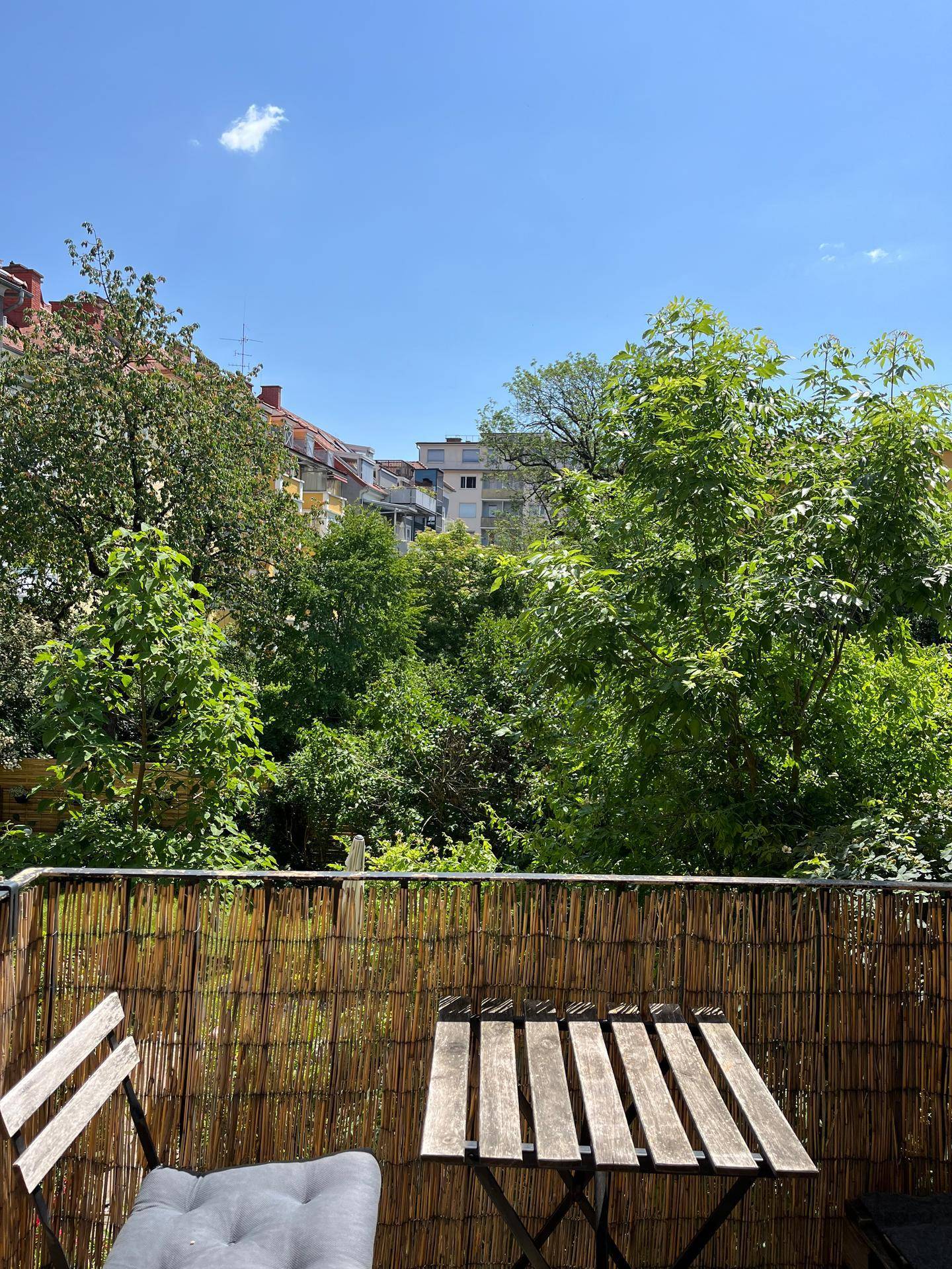 Gemütlicher Balkon mit Holztisch und Stühlen, umgeben von üppigem Grün und Bäumen.