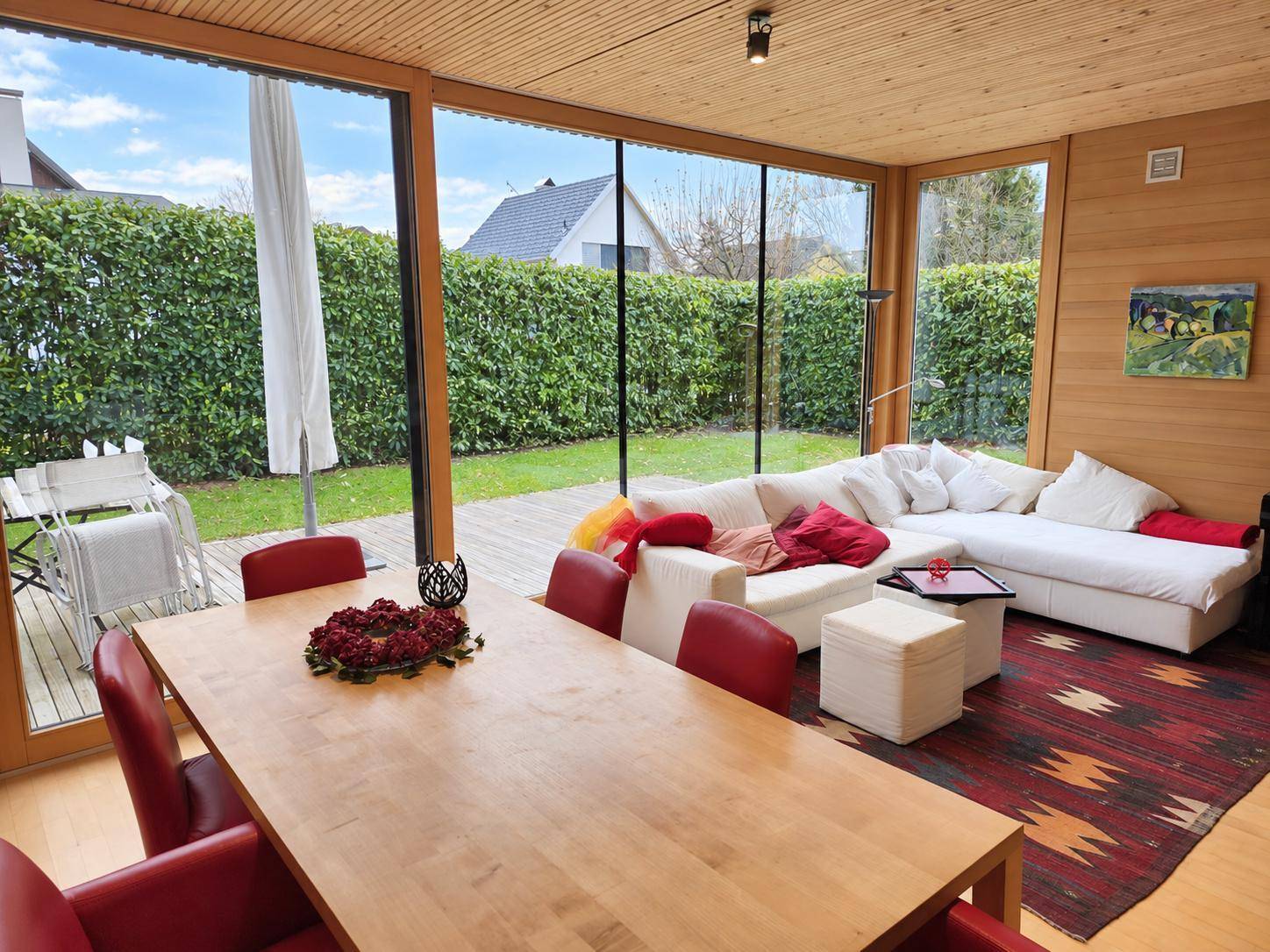 Heller Wohn- und Essbereich mit großen Glasfronten, Holzwänden und Blick in den Garten.