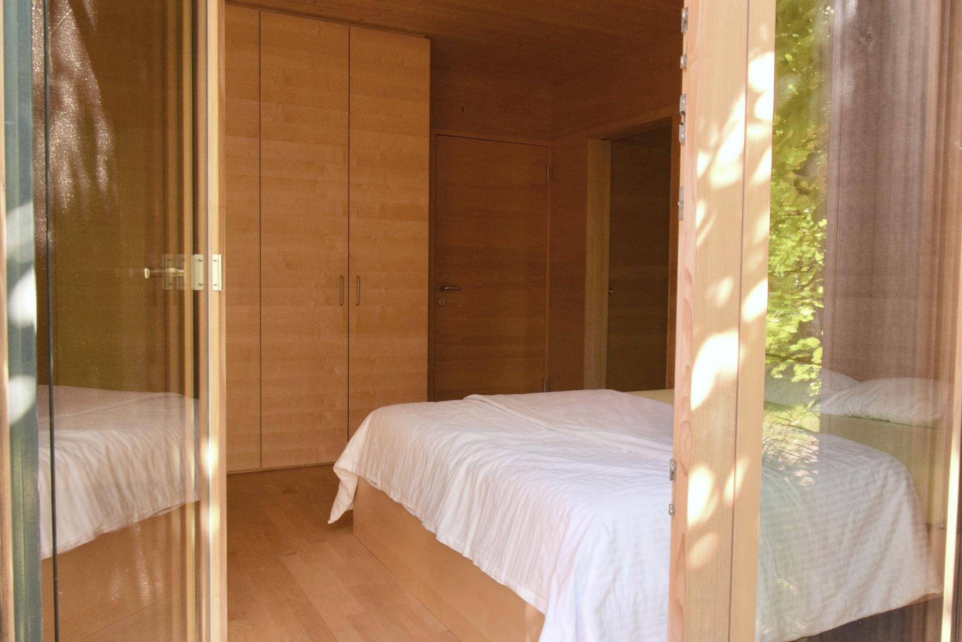Schlafzimmer mit Holzwänden, Doppelbett und Einbauschränken, hell durch Glastüren.
