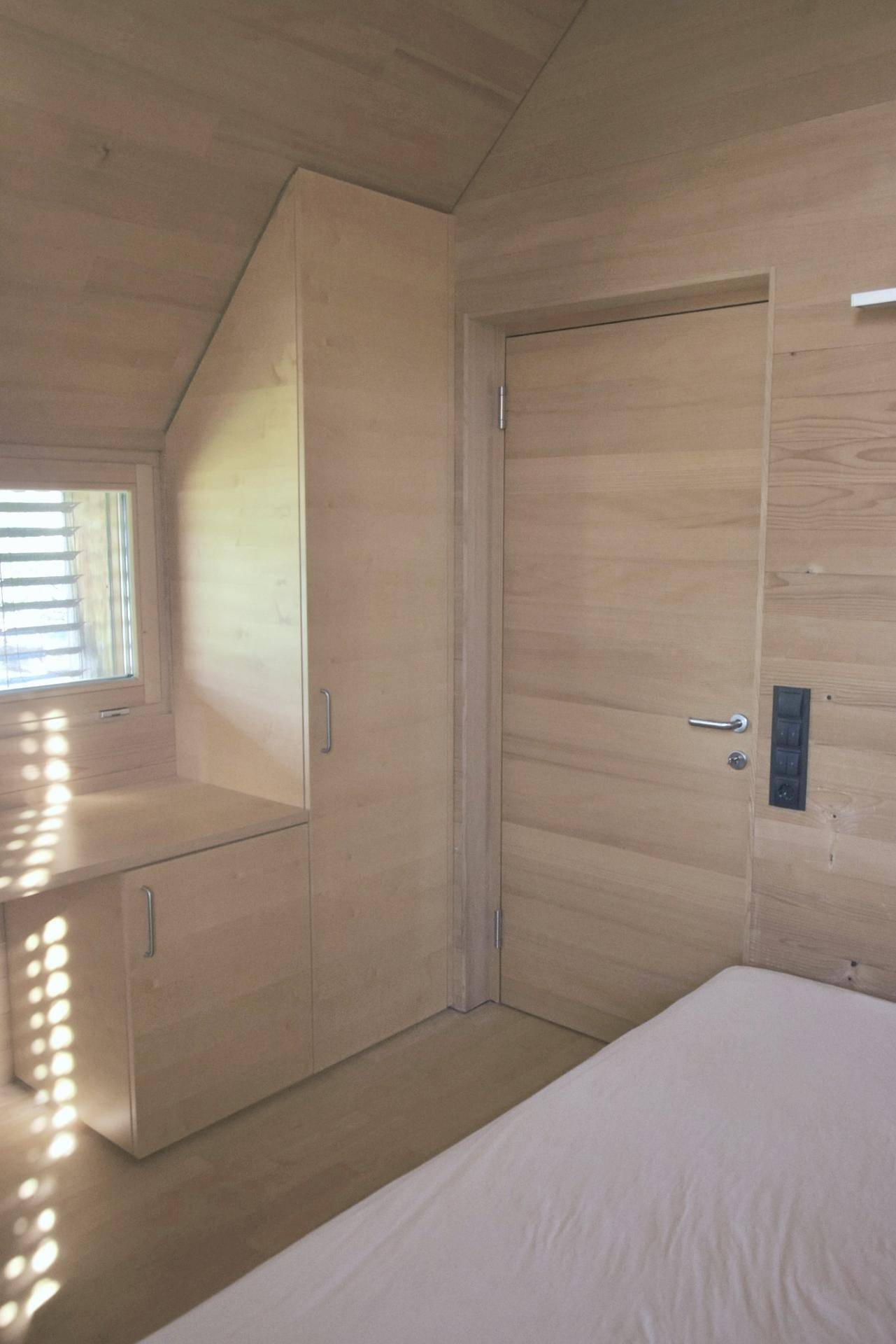 Schlafzimmer mit Holzwänden, Einbauschrank und Schreibtisch unter einem Fenster.