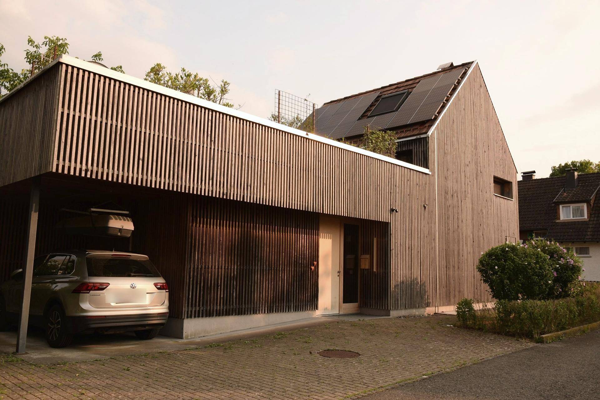 Modernes Holzhaus mit Carport und Photovoltaikanlage auf dem Dach.