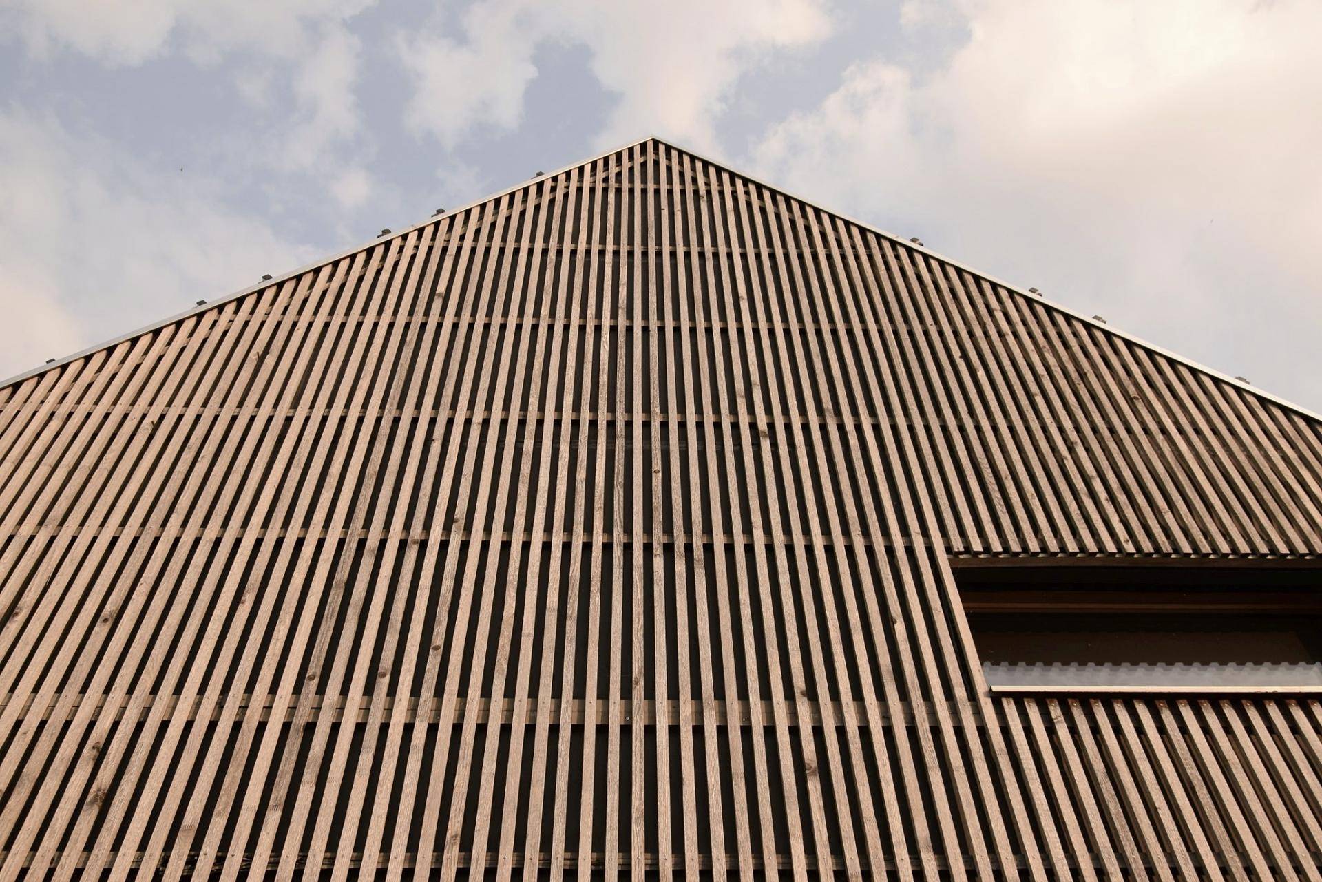Detailansicht der Holzlamellenfassade eines modernen Hauses unter bewölktem Himmel.