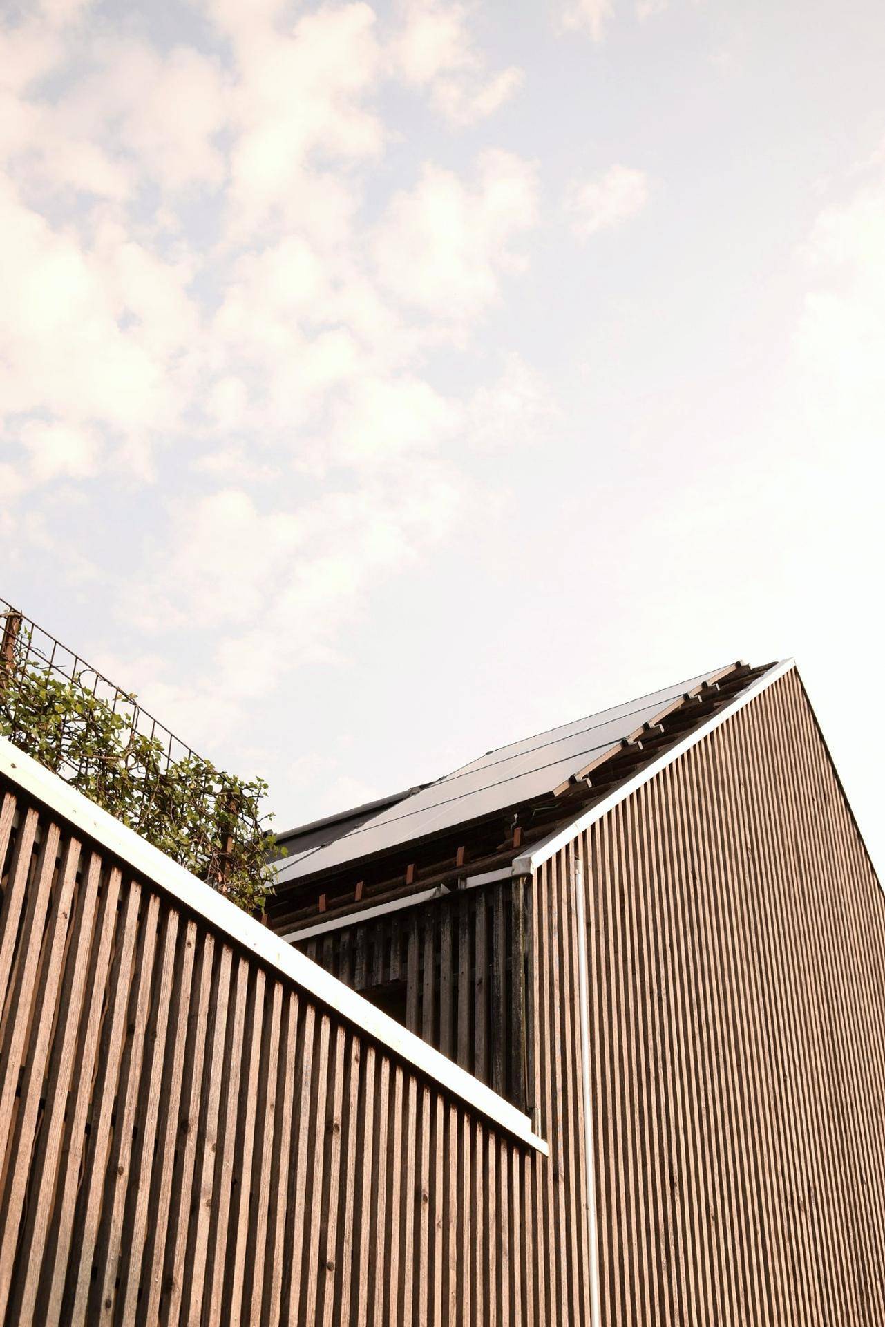 Detailansicht der Holzfassade und des Daches mit Solarpaneelen unter hellem Himmel.