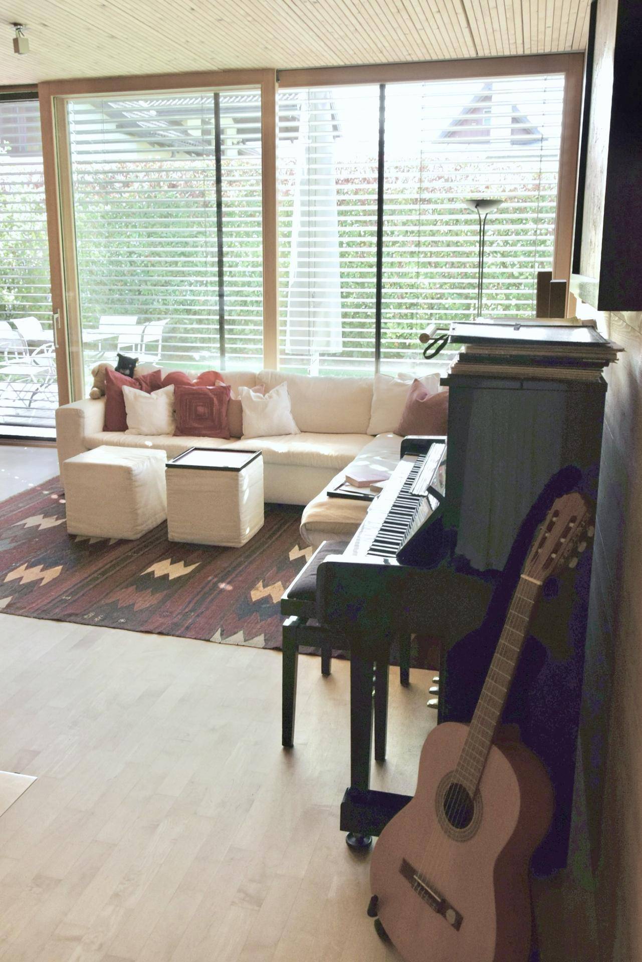 Gemütliches Wohnzimmer mit Sofa, Teppich und Musikinstrumenten, hell durch große Fenster.