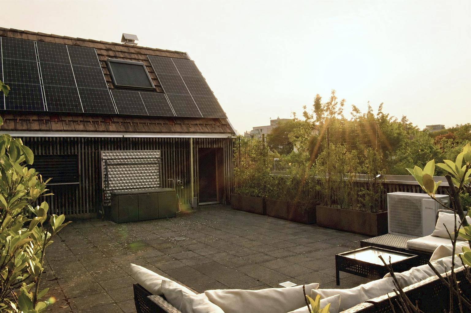Geräumige Dachterrasse mit Lounge-Möbeln und Solarpaneelen auf dem angrenzenden Dach.