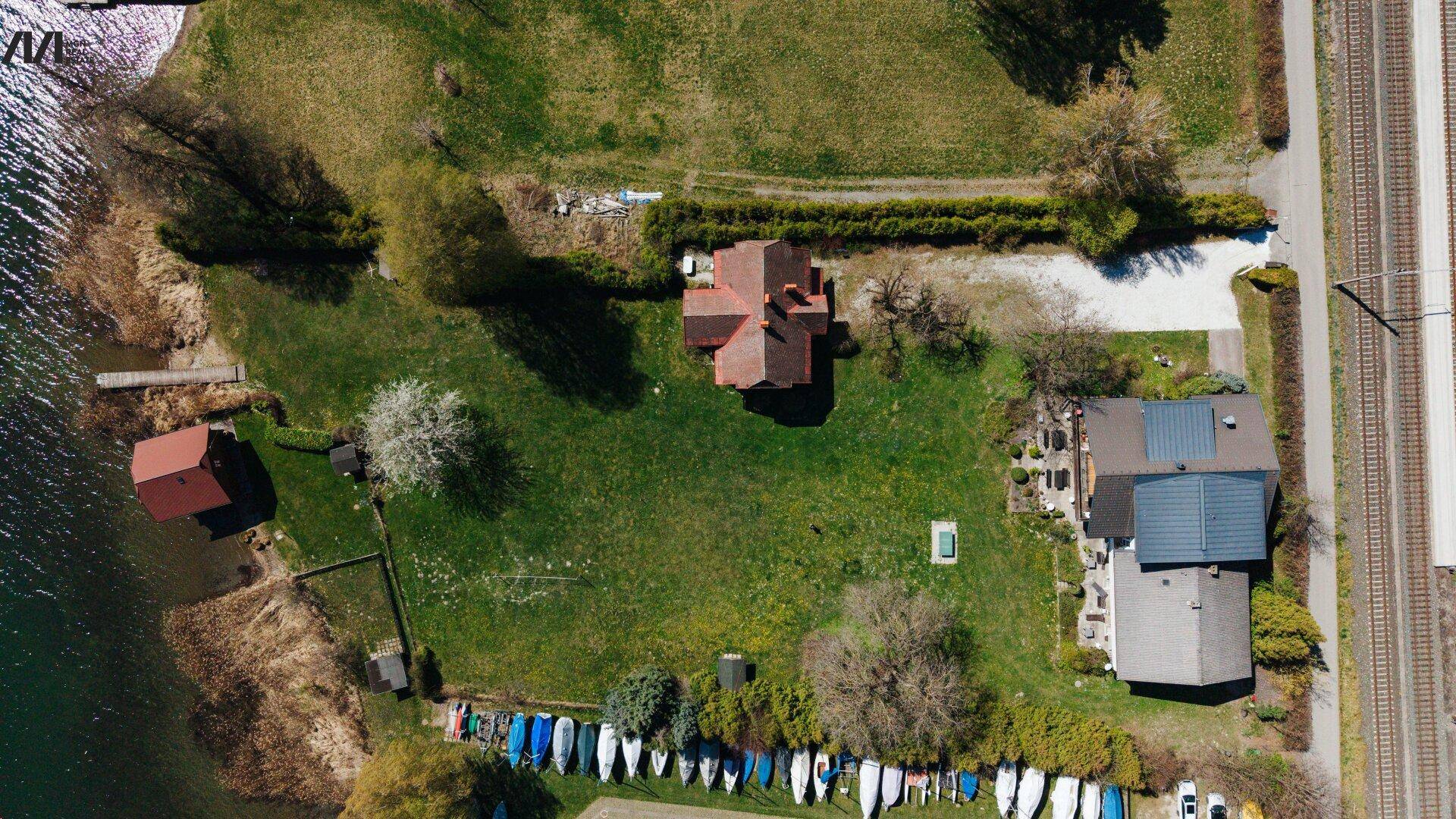 Draufsicht auf ein Seegrundstück mit Häusern, gepflegtem Garten und zahlreichen Booten am Ufer.