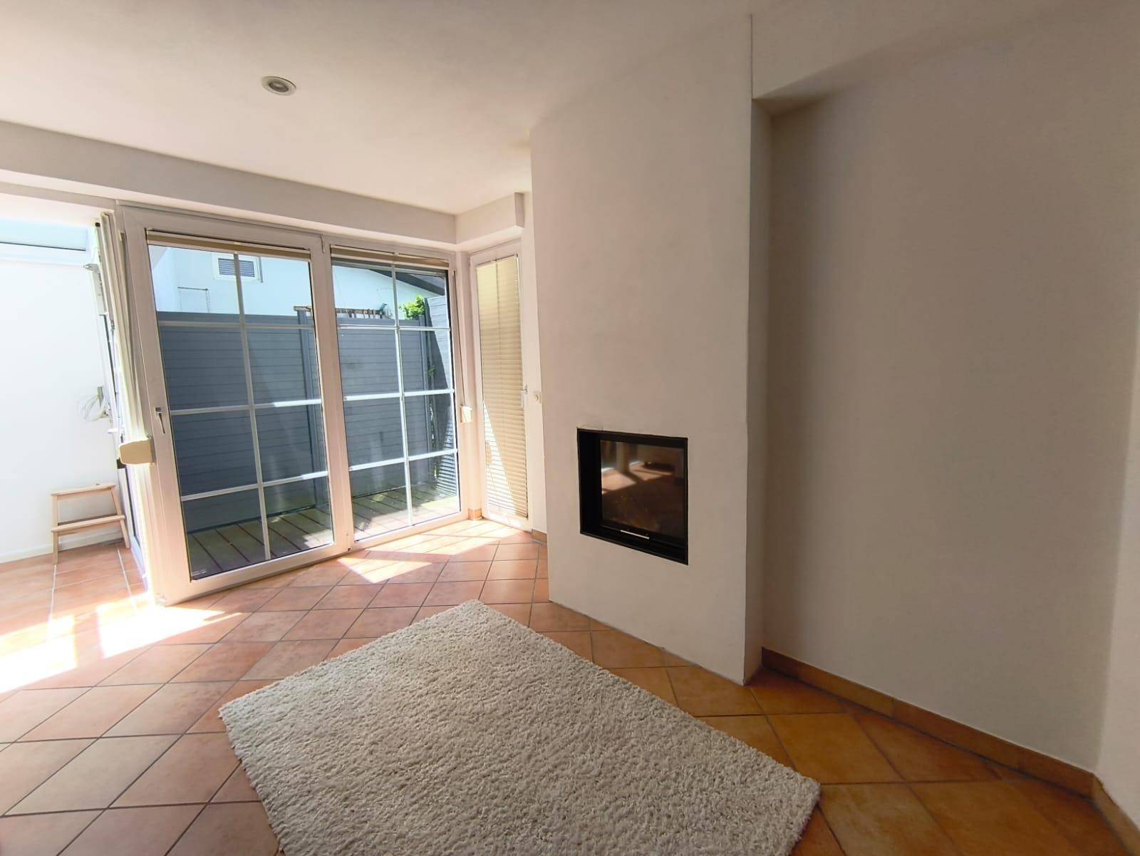 Wohnzimmer mit modernem Kamin, großen Fenstern und Terracottaboden.