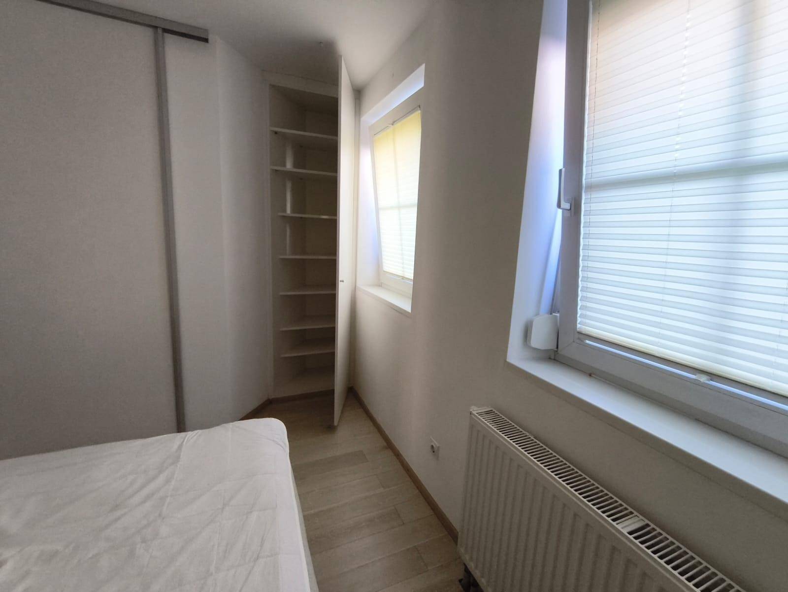 Schlafzimmer mit Fenster, Heizung und offenem Regal neben dem Einbauschrank.