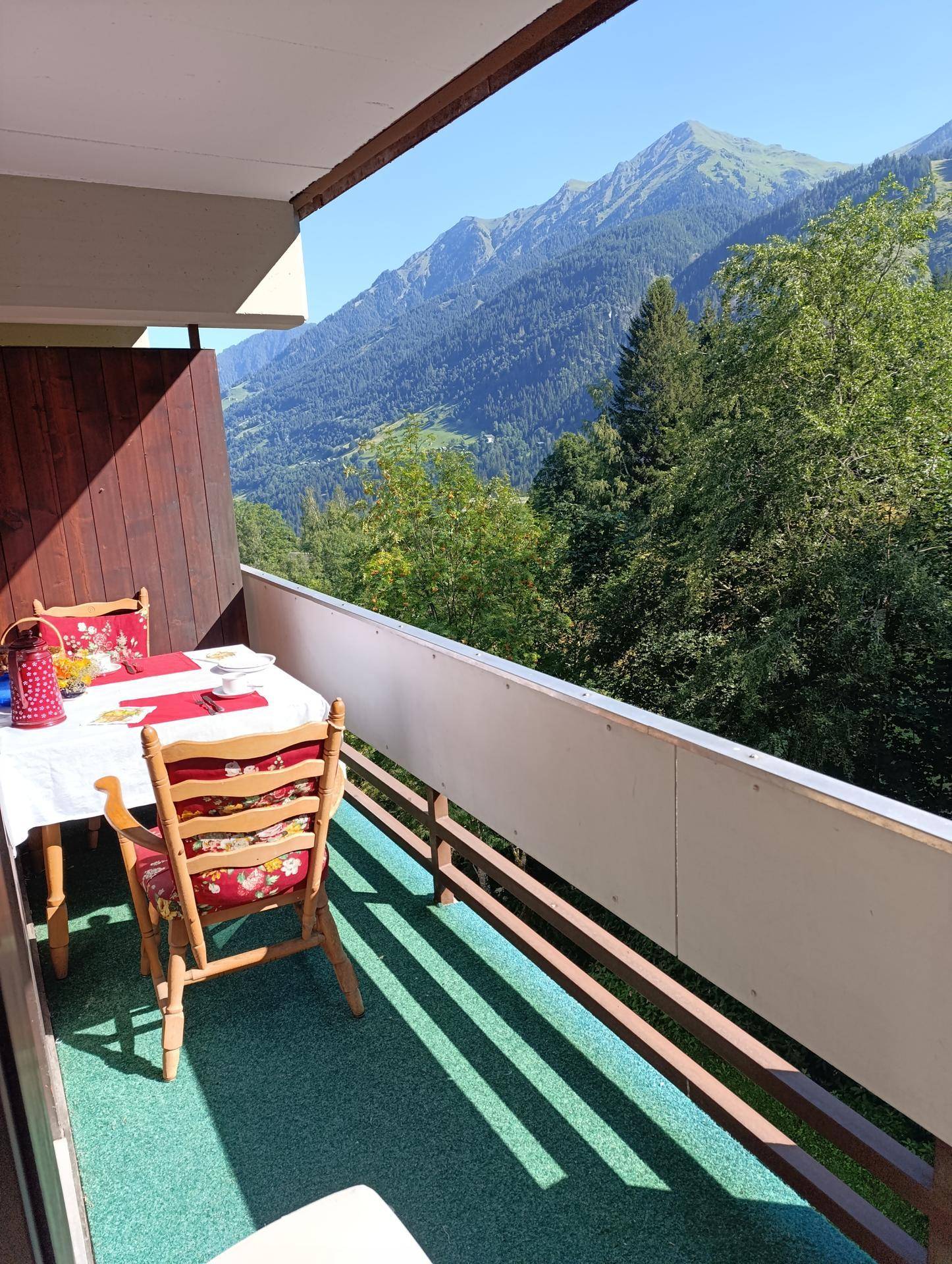 Möblierter Balkon mit Esstisch und Stühlen, bietet einen atemberaubenden Blick auf die grünen Berge.