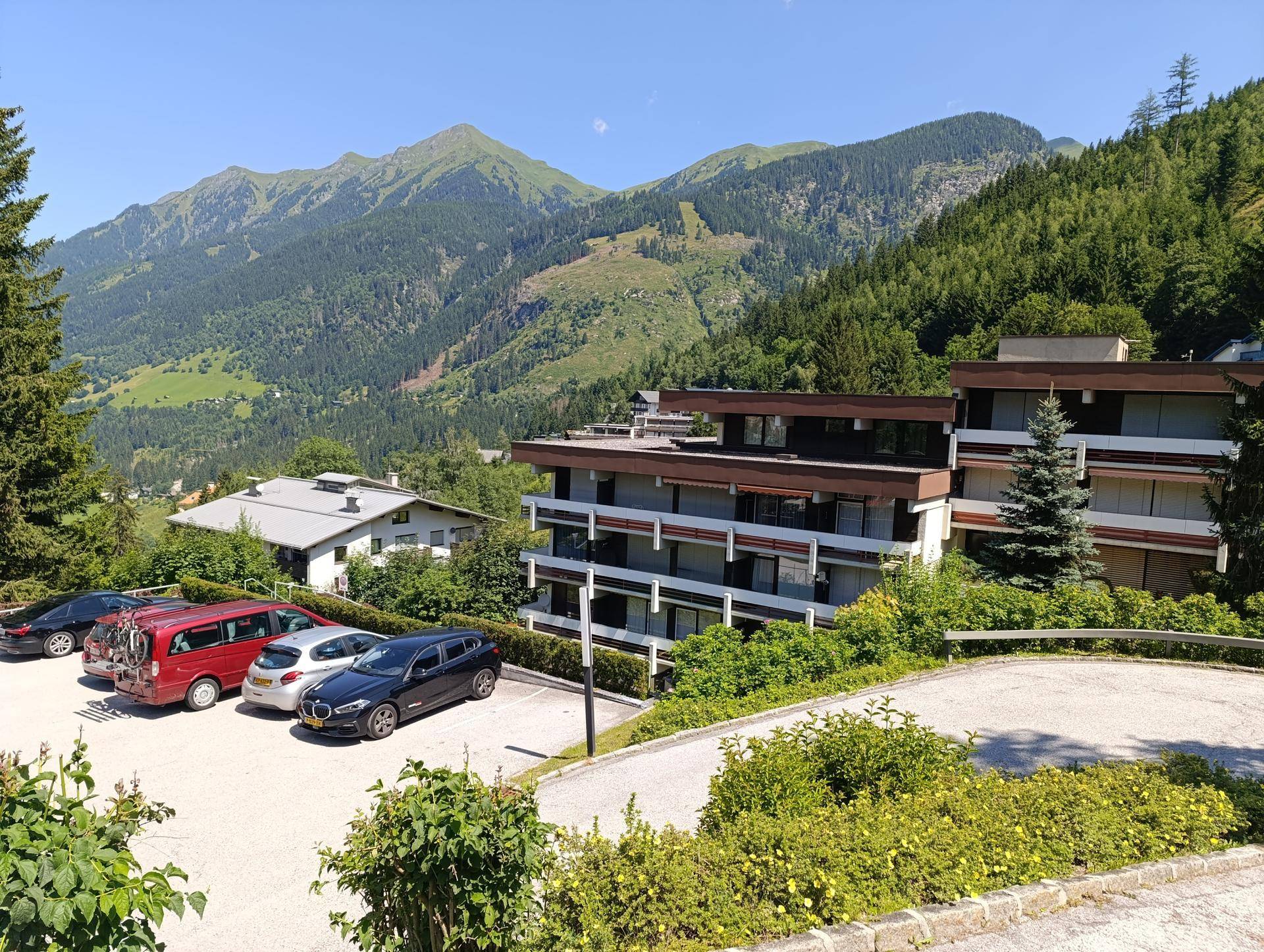 Mehrfamilienhaus mit Parkplätzen und Bergblick, umgeben von grüner Natur und Bäumen.