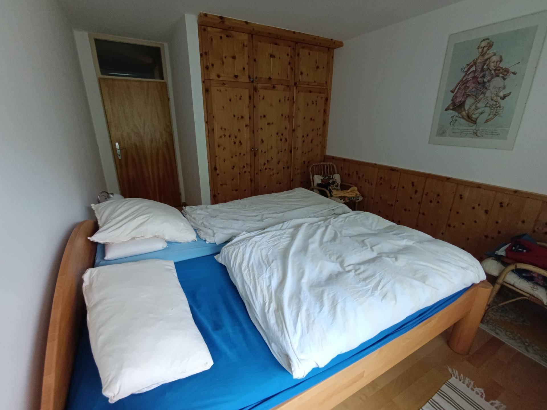 Gemütliches Schlafzimmer mit Holzbett, großem Einbauschrank und rustikaler Holzvertäfelung. Die hellen Wände ergänzen den Holzboden.