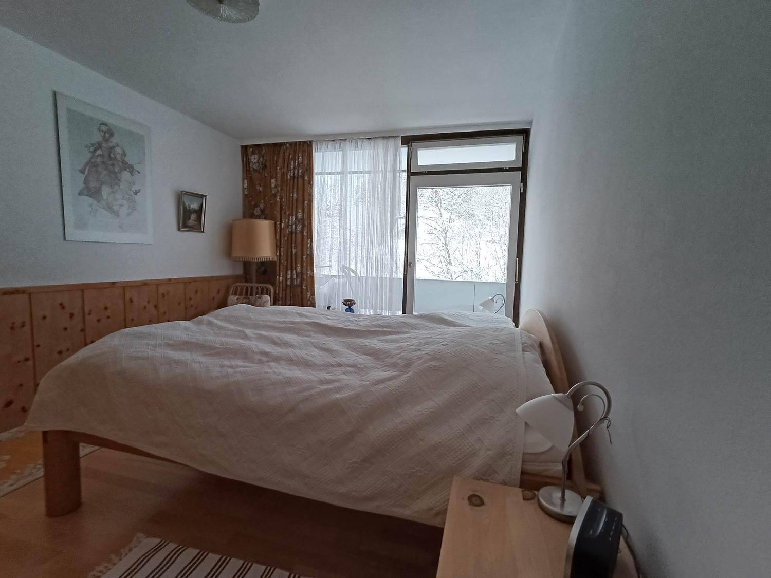 Gemütliches Schlafzimmer mit Holzbett, Holzvertäfelung und direktem Zugang zum Balkon, umgeben von Natur.