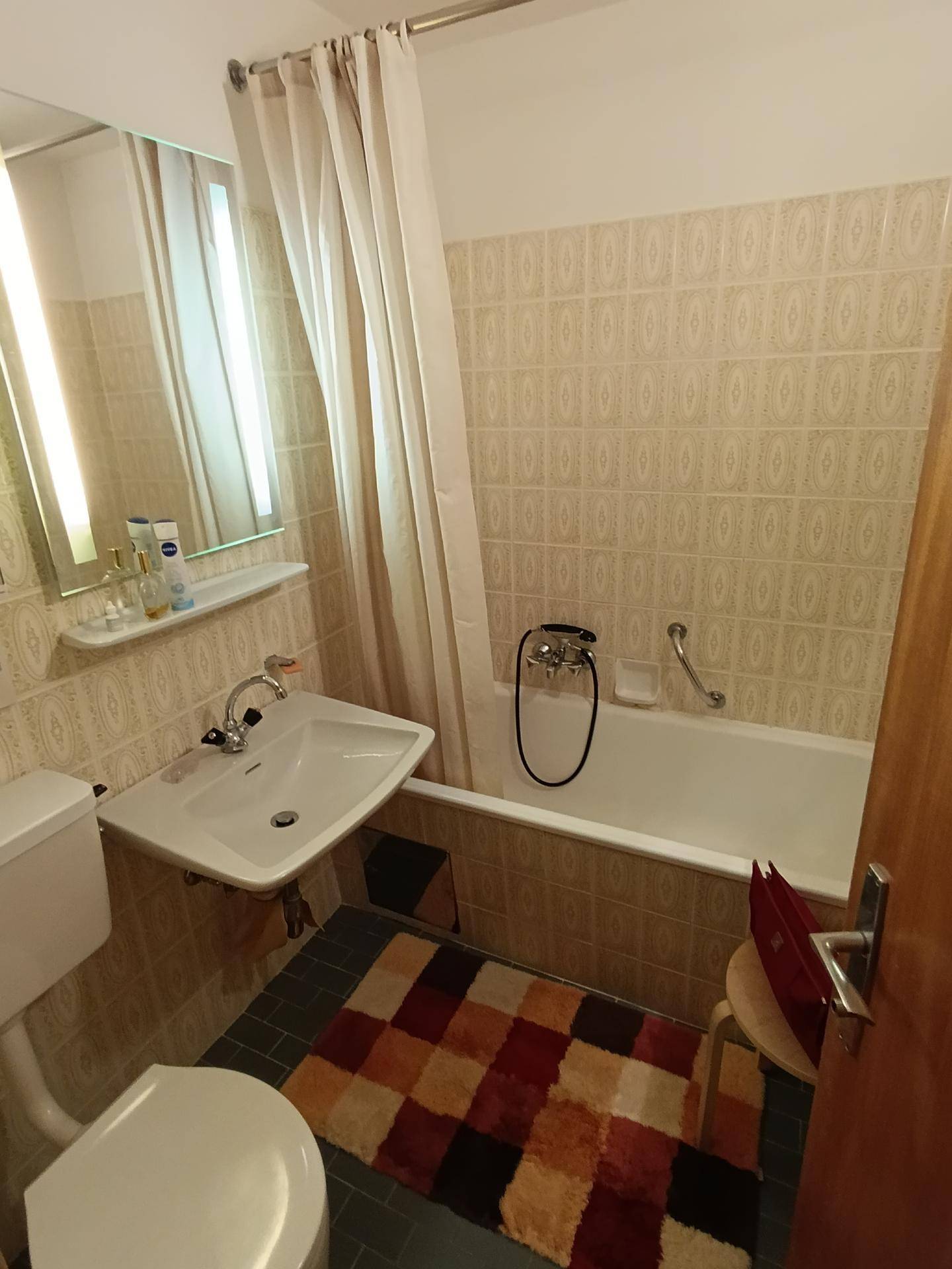Badezimmer mit Badewanne, Waschbecken und WC, ausgestattet mit gemusterten Fliesen und Duschvorhang.