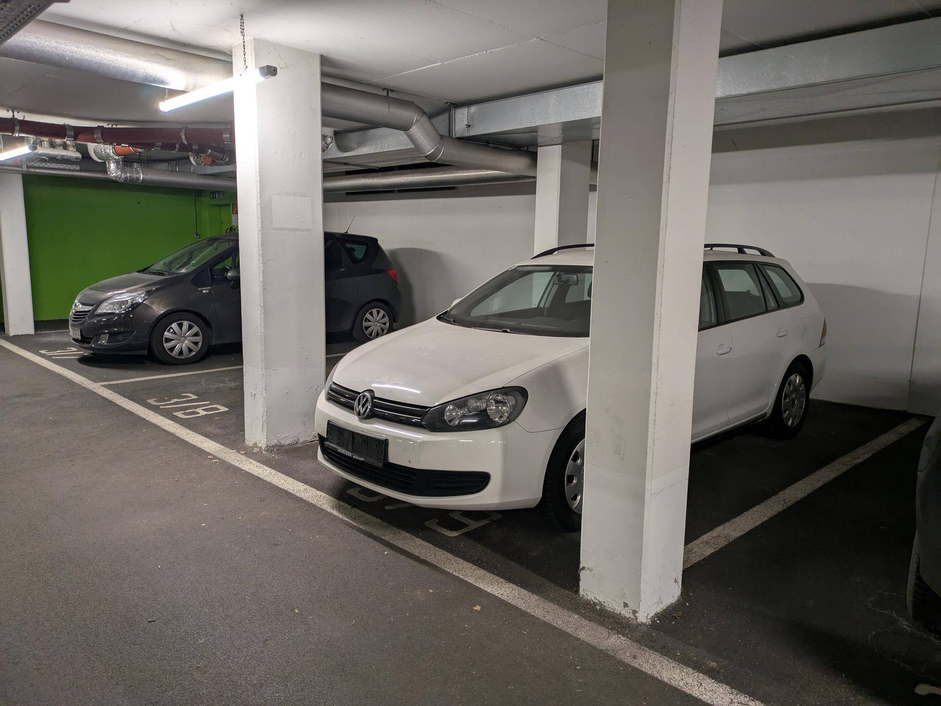 Blick auf einen Parkplatz in einer Tiefgarage mit einem weißen Kombi und weiteren Fahrzeugen.