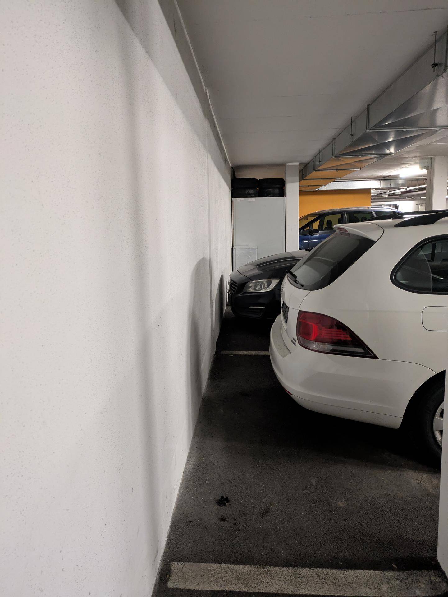 Enger Bereich in einer Tiefgarage zwischen einer Wand und geparkten Fahrzeugen.