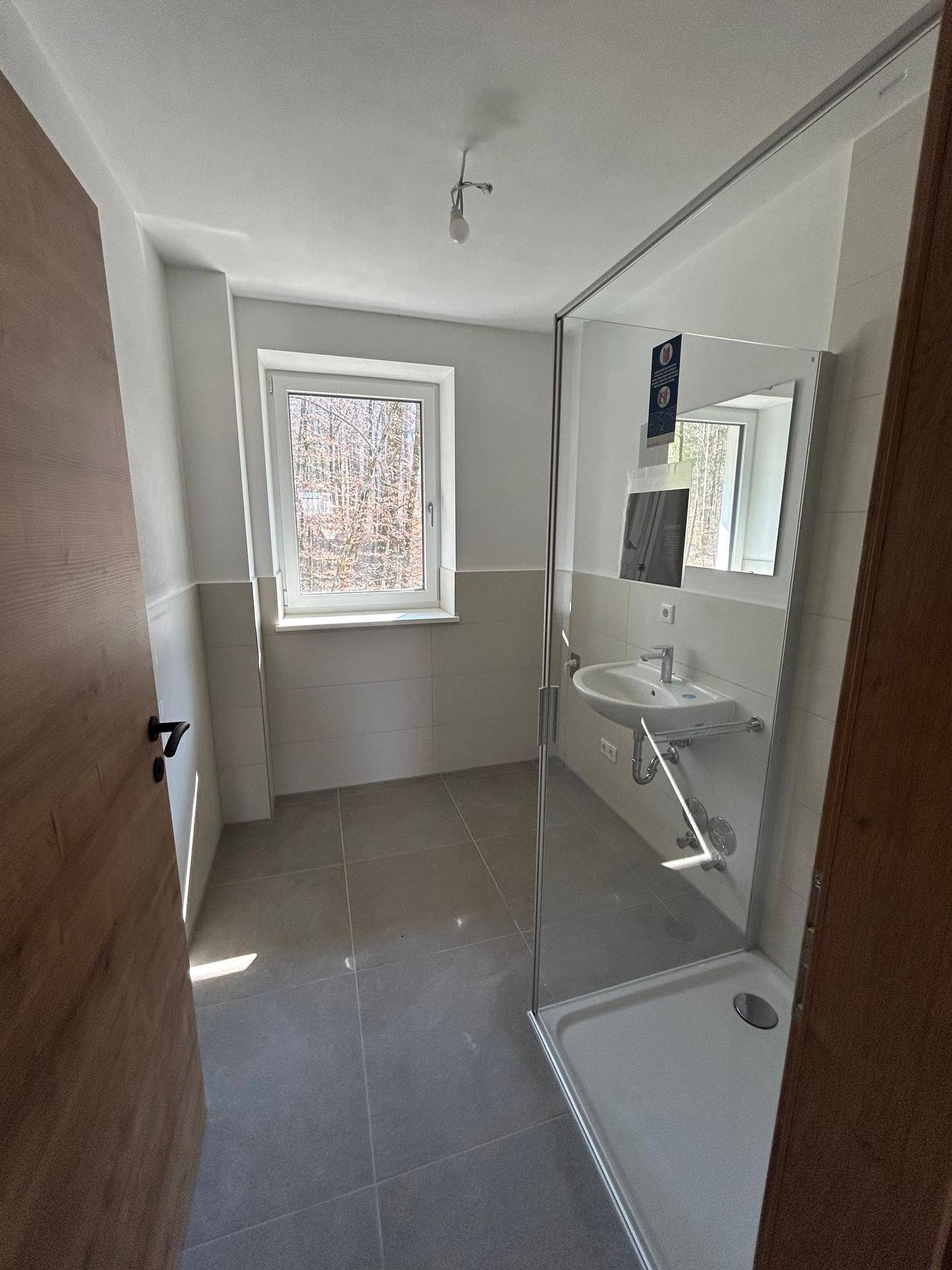 Modernes Badezimmer mit Fenster, Duschkabine und hellen Fliesen, die den Raum aufhellen und einladend wirken.