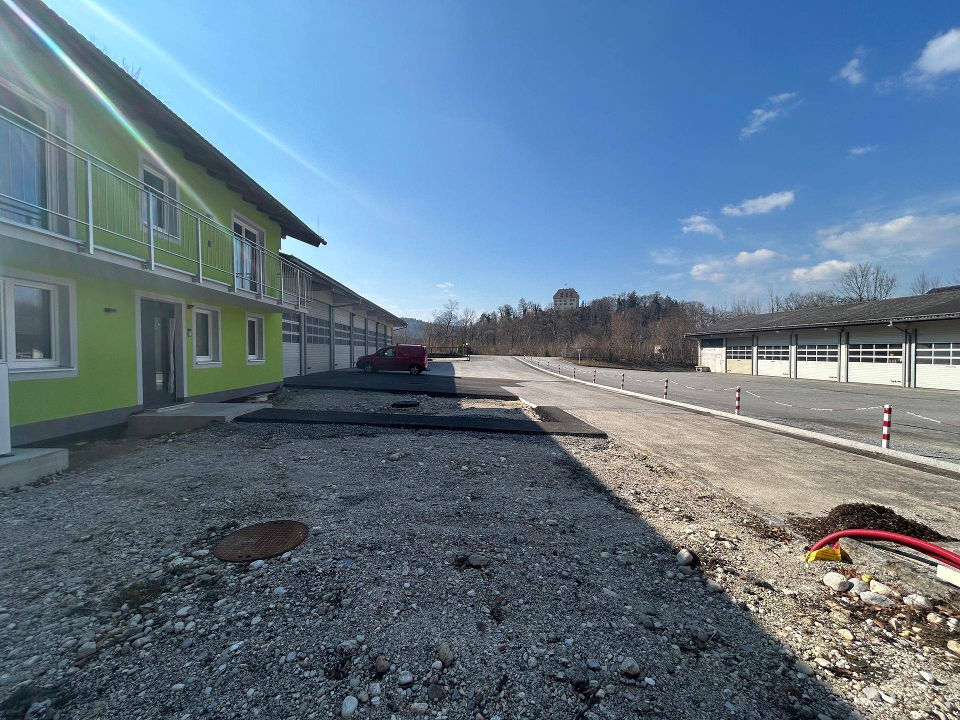 Gesamtansicht des grünen Gebäudes und der Garagenanlage mit weitem Blick auf die hügelige Umgebung.