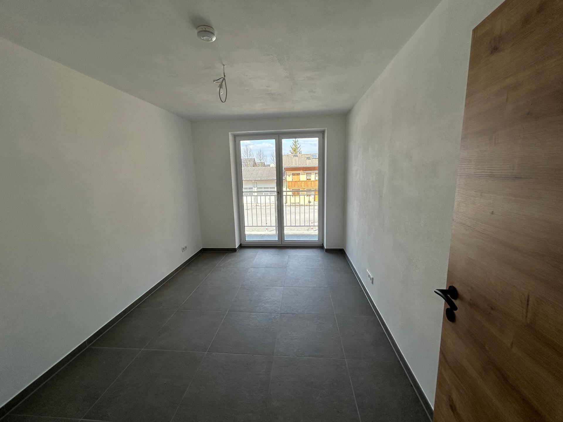 Heller Raum mit Zugang zu einem Balkon und grauen Fliesen, ideal für Wohnzwecke und mit viel Tageslicht.