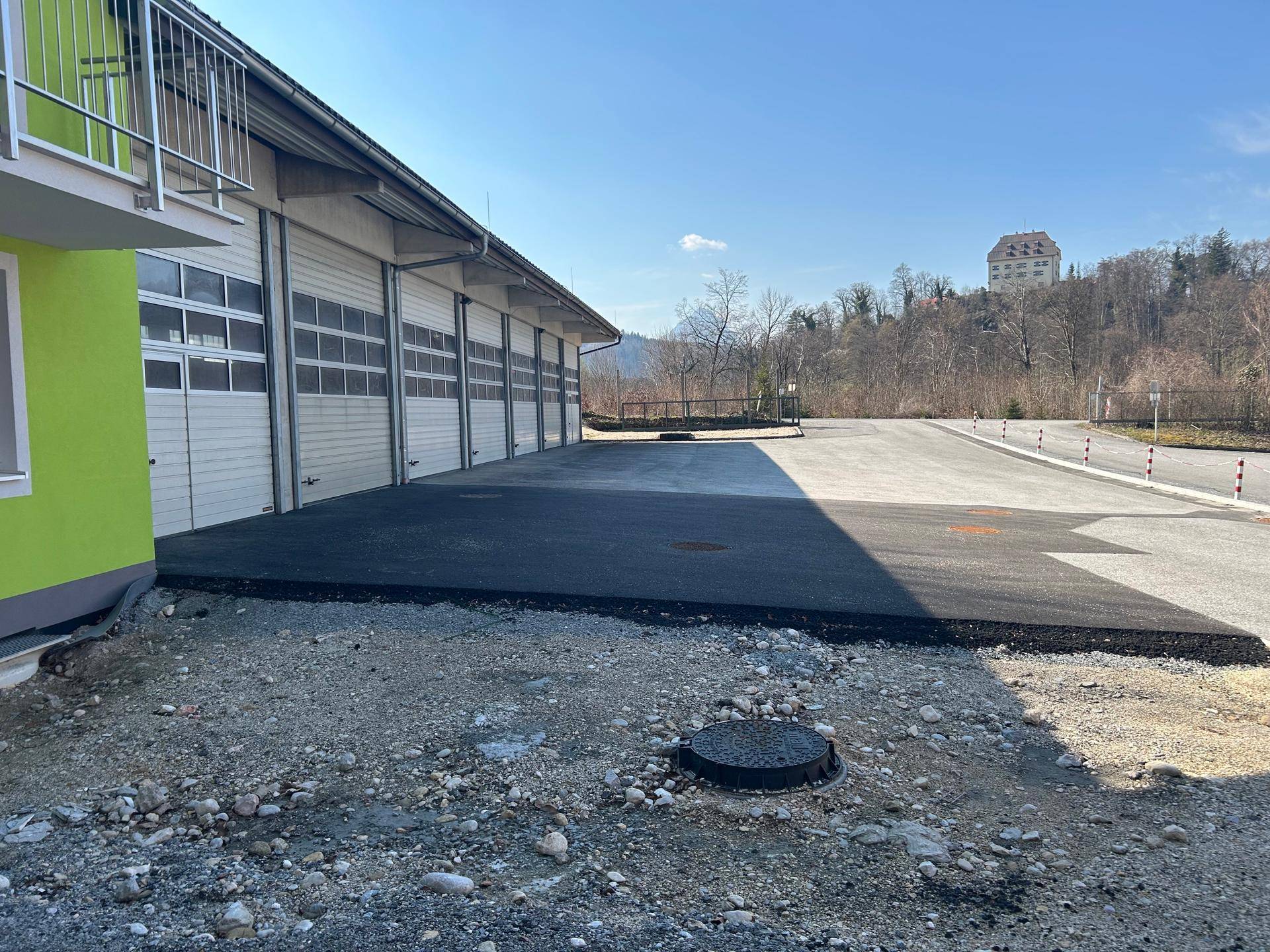 Ansicht der Garagengebäude mit frisch asphaltierter Fläche und Blick auf die hügelige Landschaft im Hintergrund.