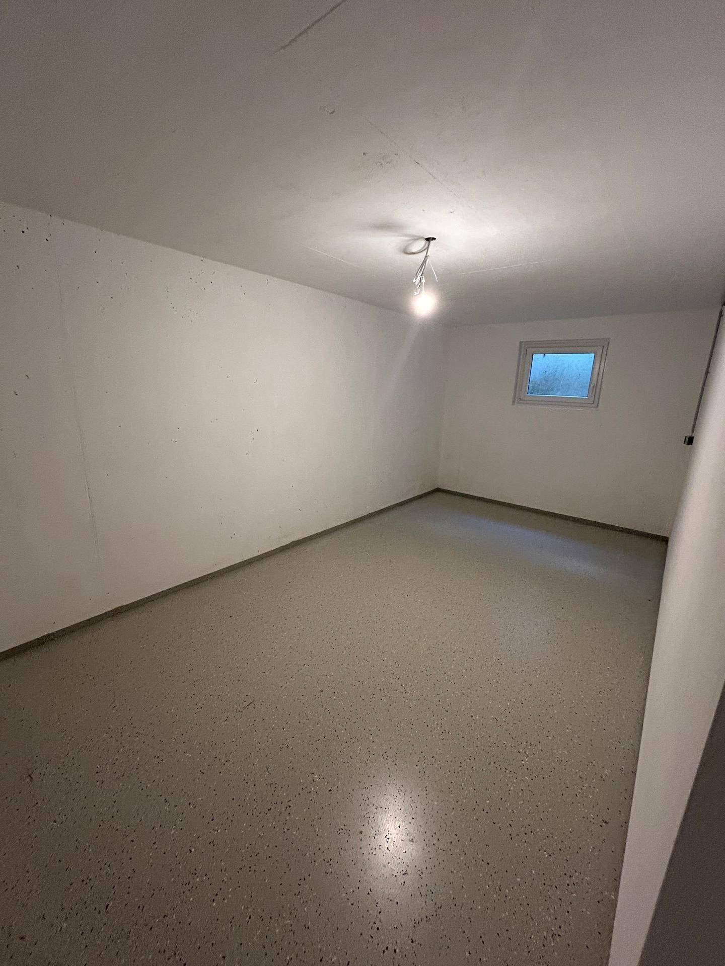 Geräumiger Kellerraum mit kleinem Fenster und strapazierfähigem Boden, ideal als Abstellraum oder Hobbyraum.