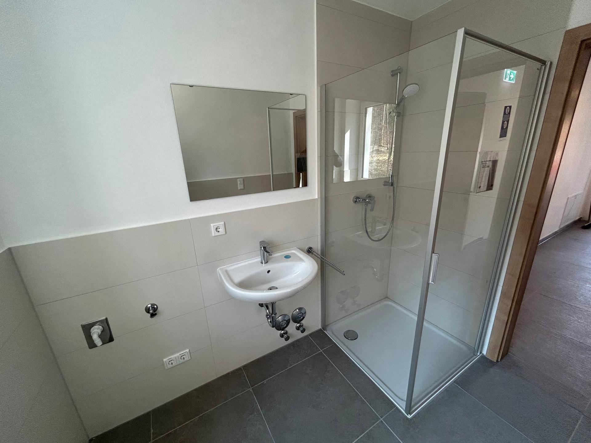 Modernes Badezimmer mit Duschkabine, Waschbecken und hellen Fliesen an Wänden und Boden, sehr gepflegt.