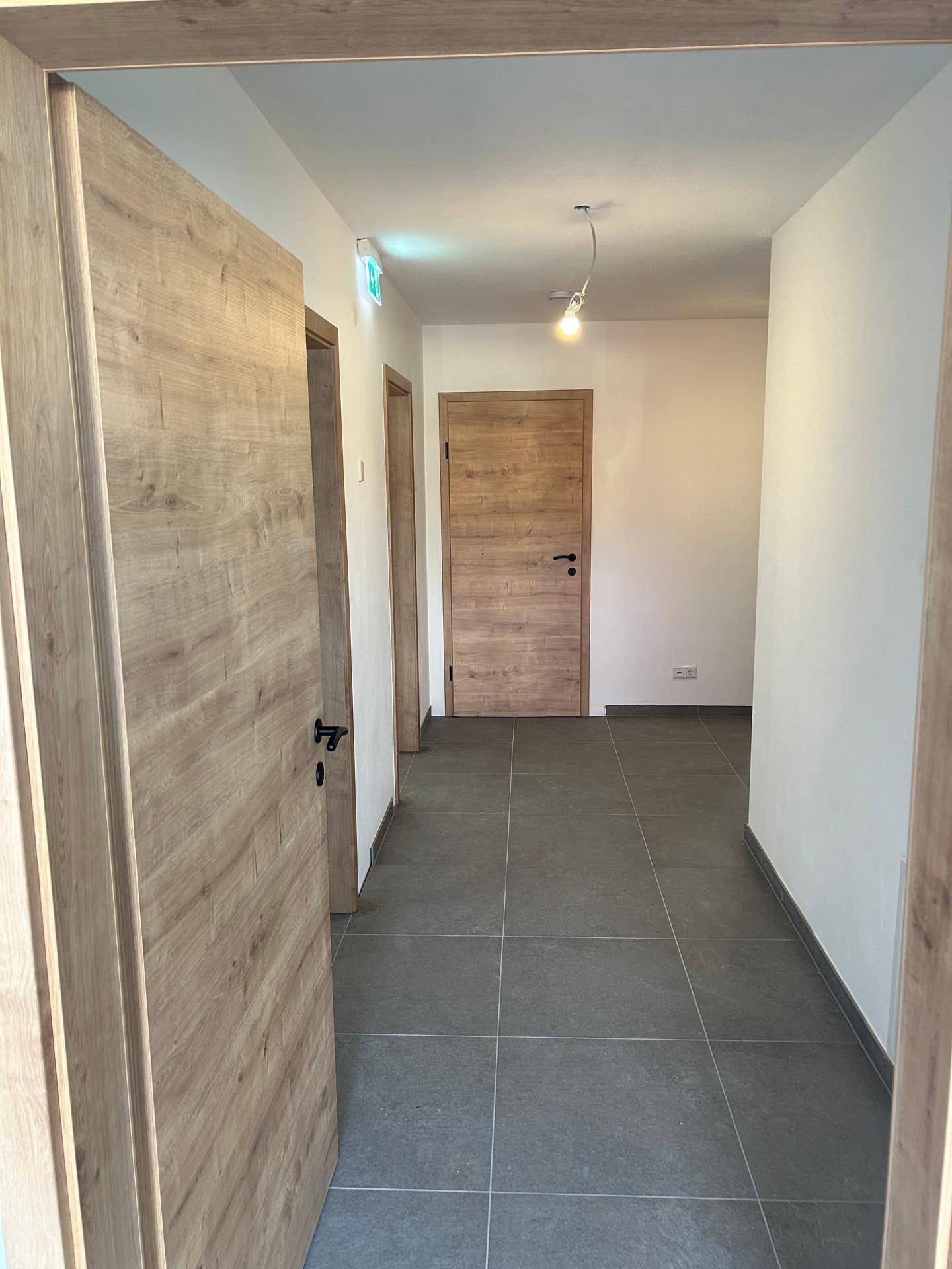 Heller Flur mit modernen Holztüren und grauen Fliesen, der zu verschiedenen Räumen im Gebäude führt.