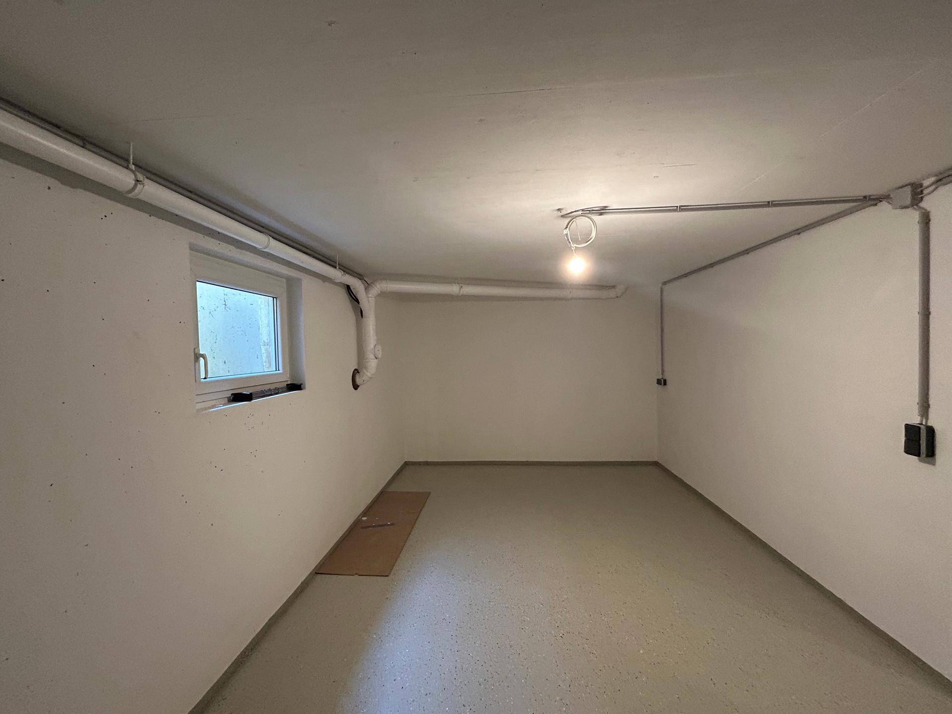 Kellerraum mit sichtbaren Leitungen, kleinem Fenster und robustem Boden, vielseitig nutzbar für Lagerung.