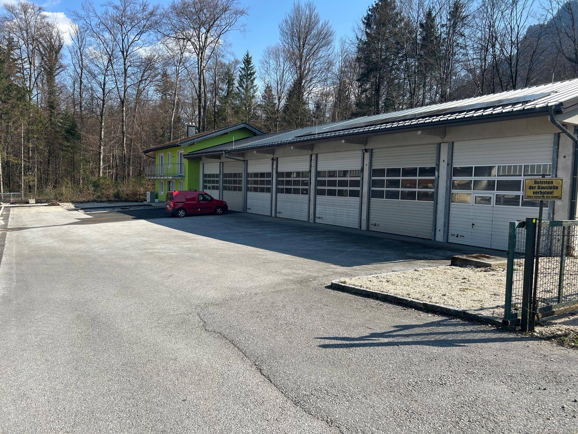 Weitläufige Außenansicht eines modernen Gebäudes mit Garagen und großem asphaltierten Parkplatz unter blauem Himmel.