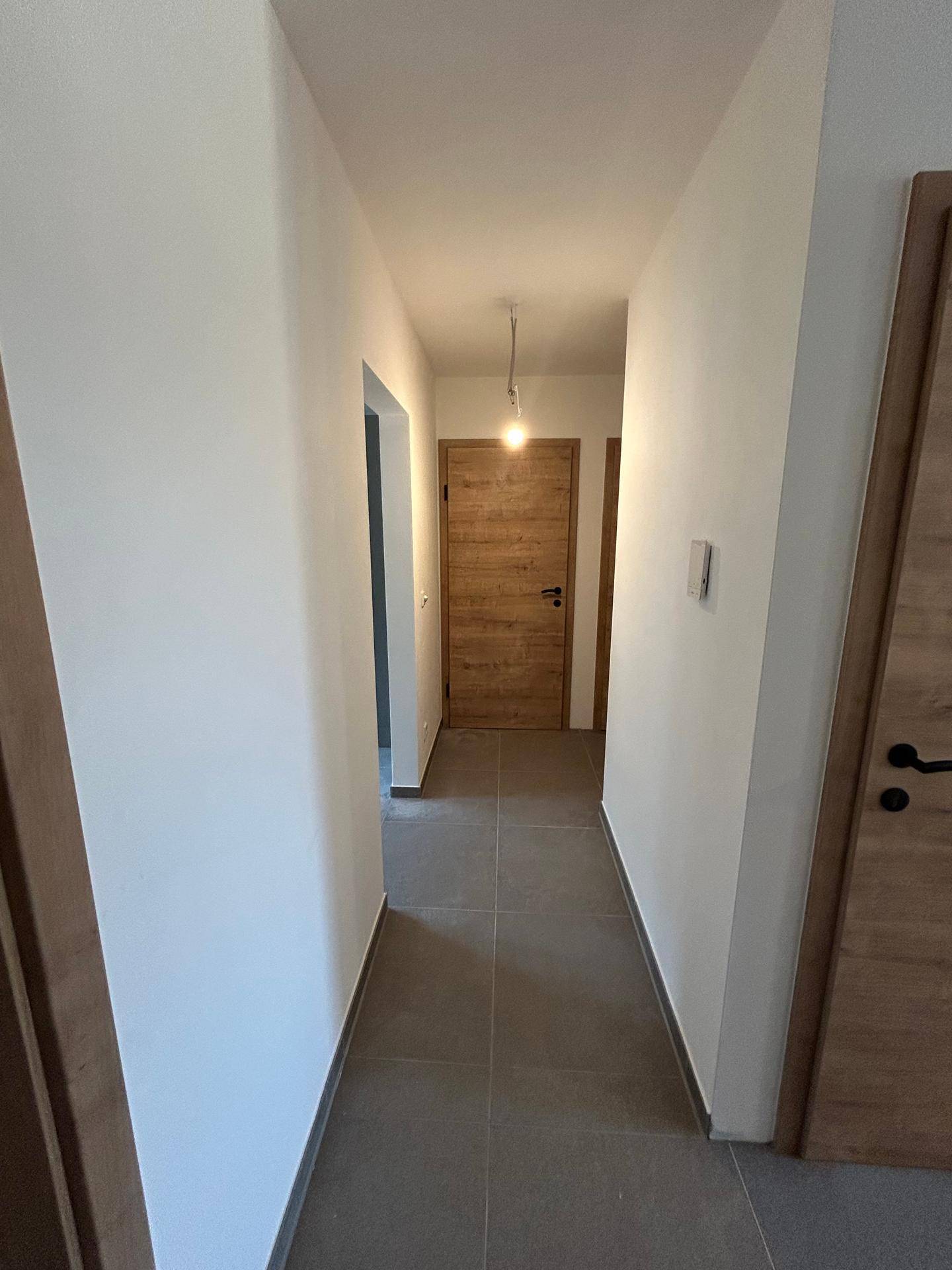 Moderner Flur mit Holztüren und grauen Fliesen, der eine einladende und gepflegte Atmosphäre schafft.