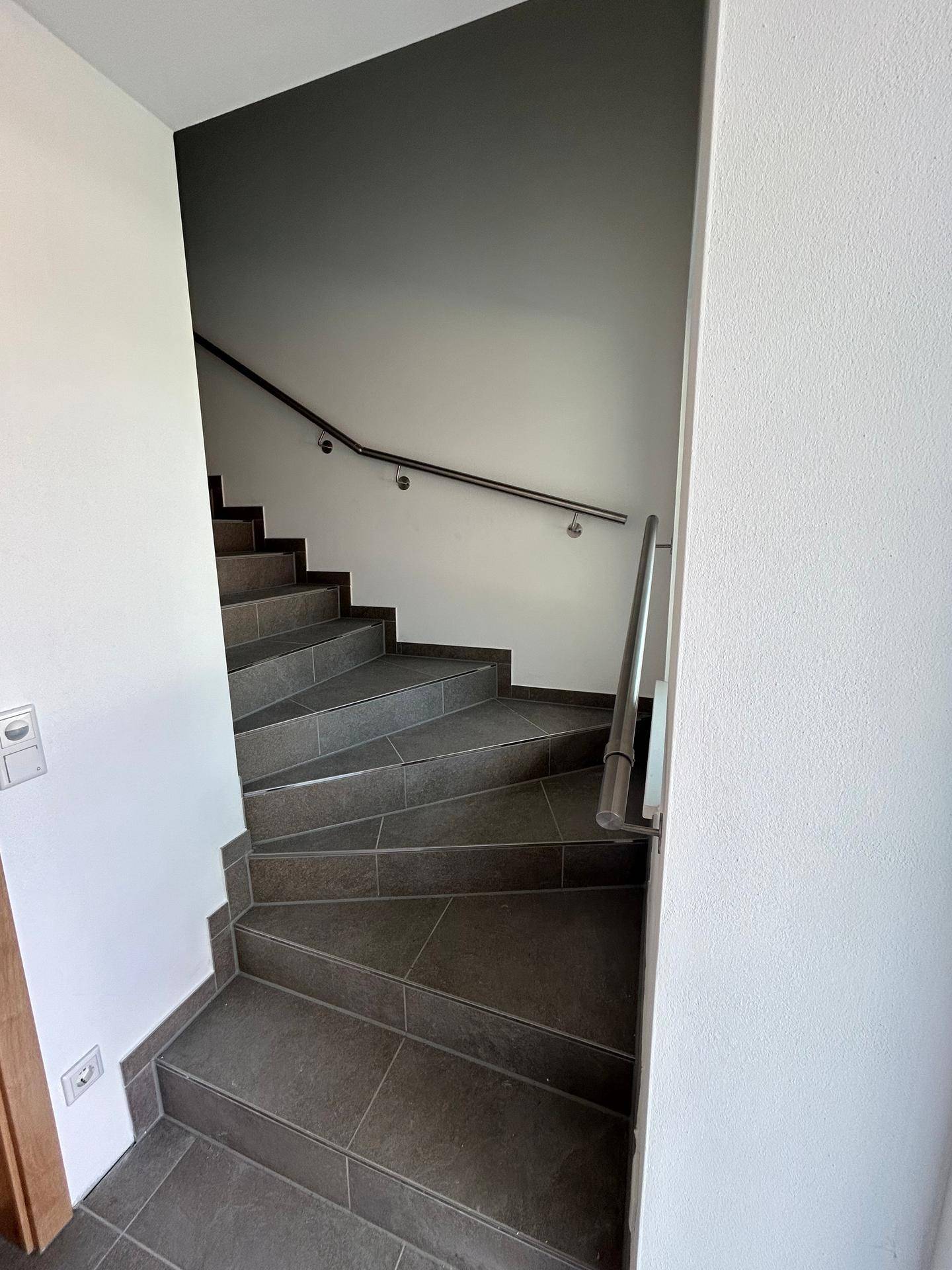 Moderne Treppe mit grauen Fliesenstufen und einem eleganten Edelstahlgeländer, das Sicherheit bietet.
