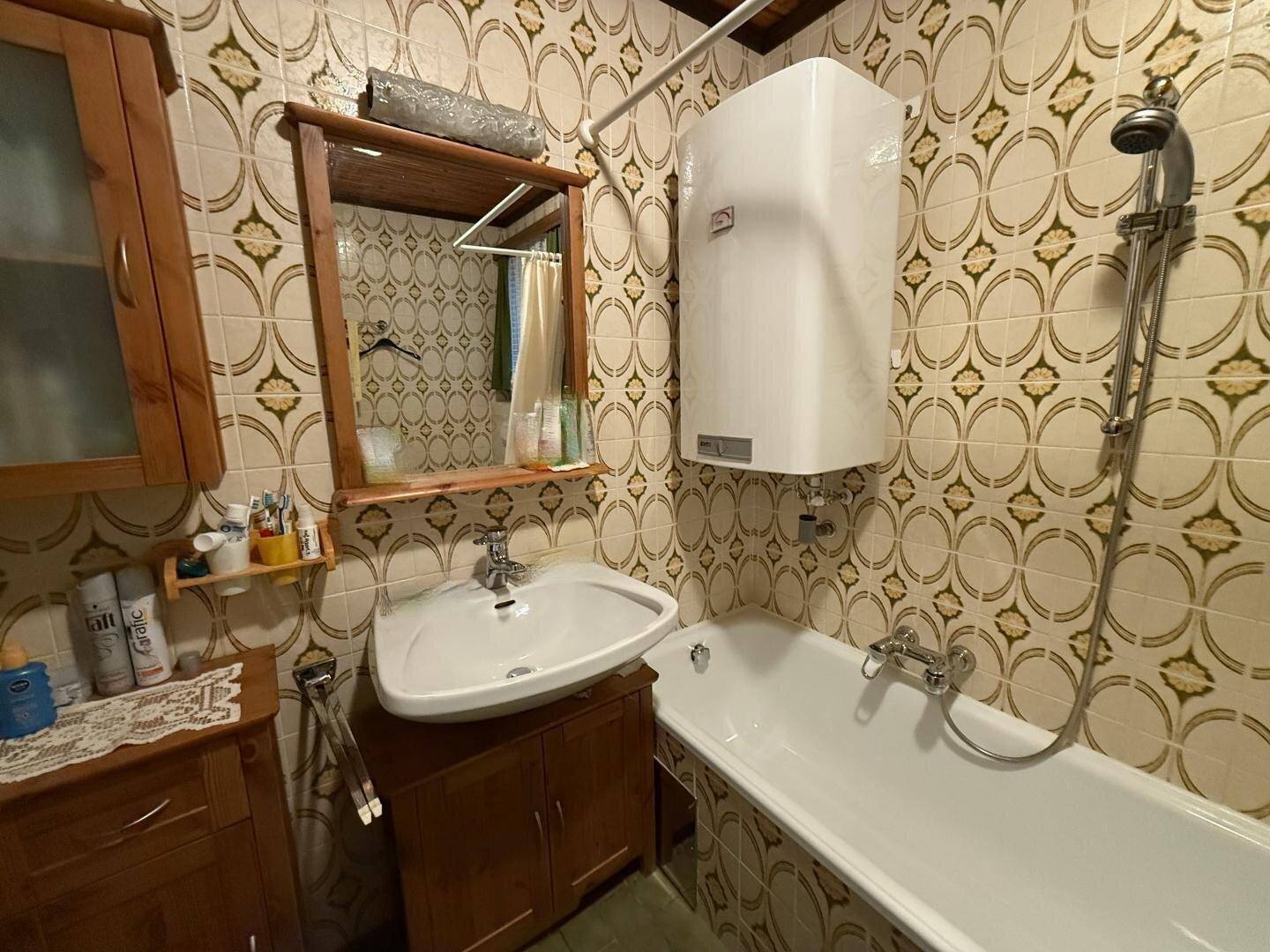 Badezimmer mit Badewanne, Waschbecken und Wandfliesen im Retro-Stil.