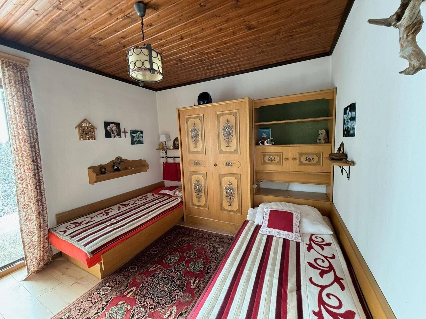 Kinder- oder Gästezimmer mit zwei Einzelbetten, Holzdecke und Blick ins Grüne.