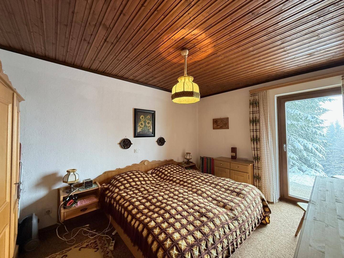 Schlafzimmer mit Doppelbett, Holzdecke und Zugang zu einem Balkon oder Garten.