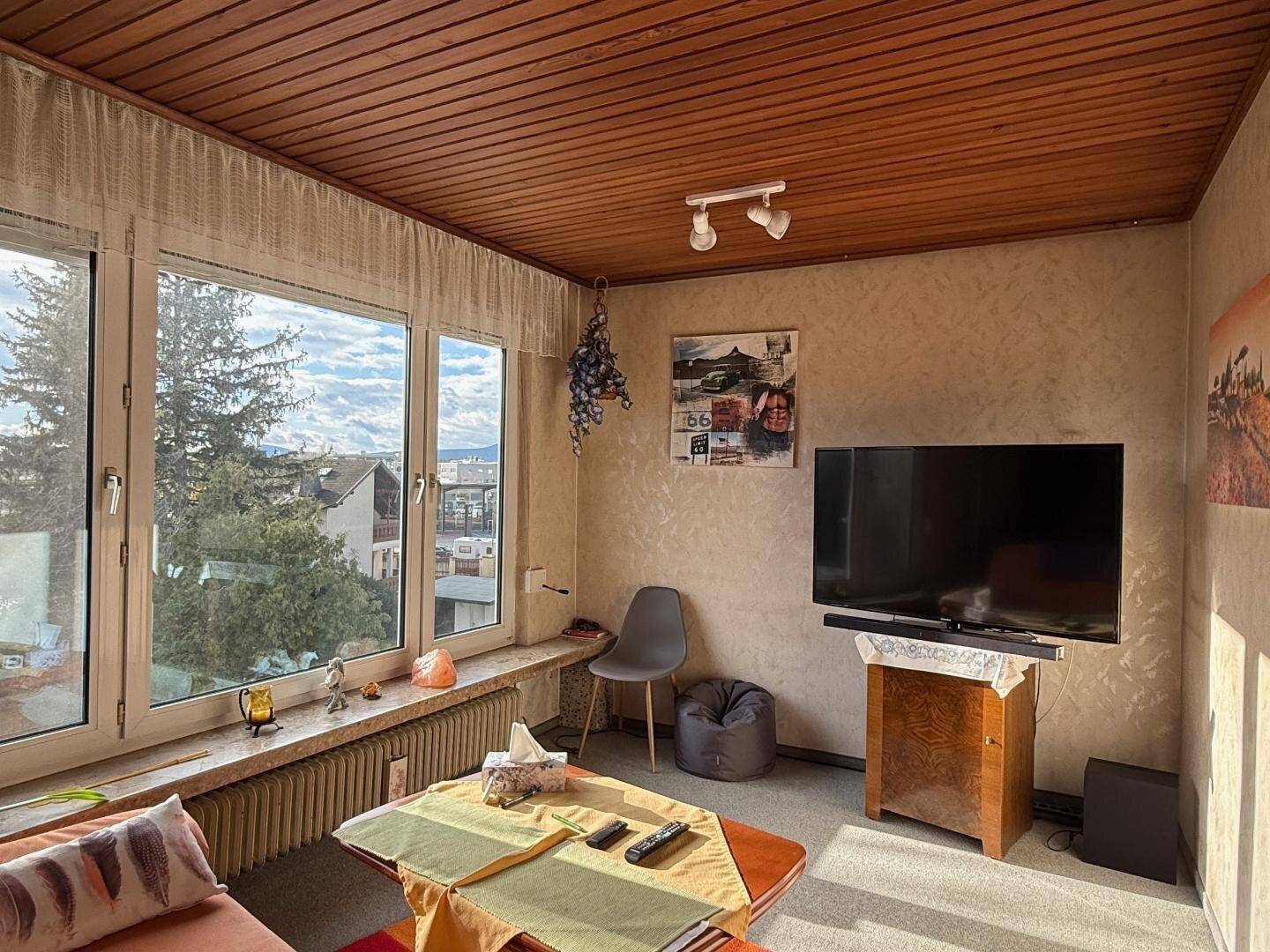 Helles Wohnzimmer mit Holzdecke, großen Fenstern und einem weiten Blick über die Umgebung.