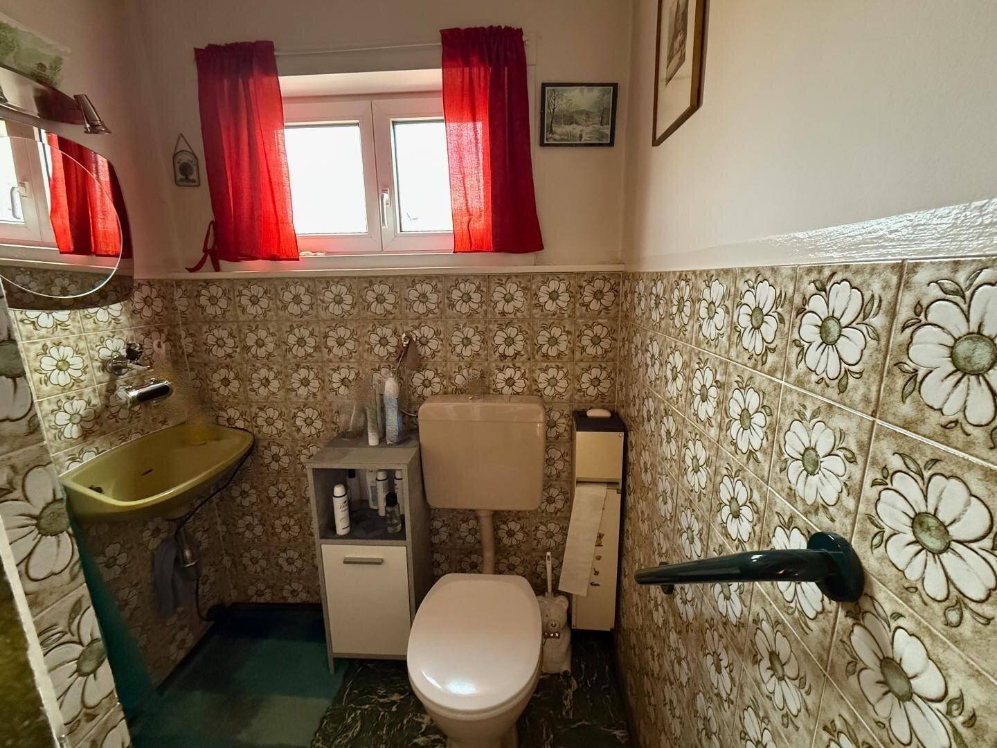 Badezimmer im Stil der 80er Jahre mit floralen Fliesen, Toilette, Waschbecken und Fenster.