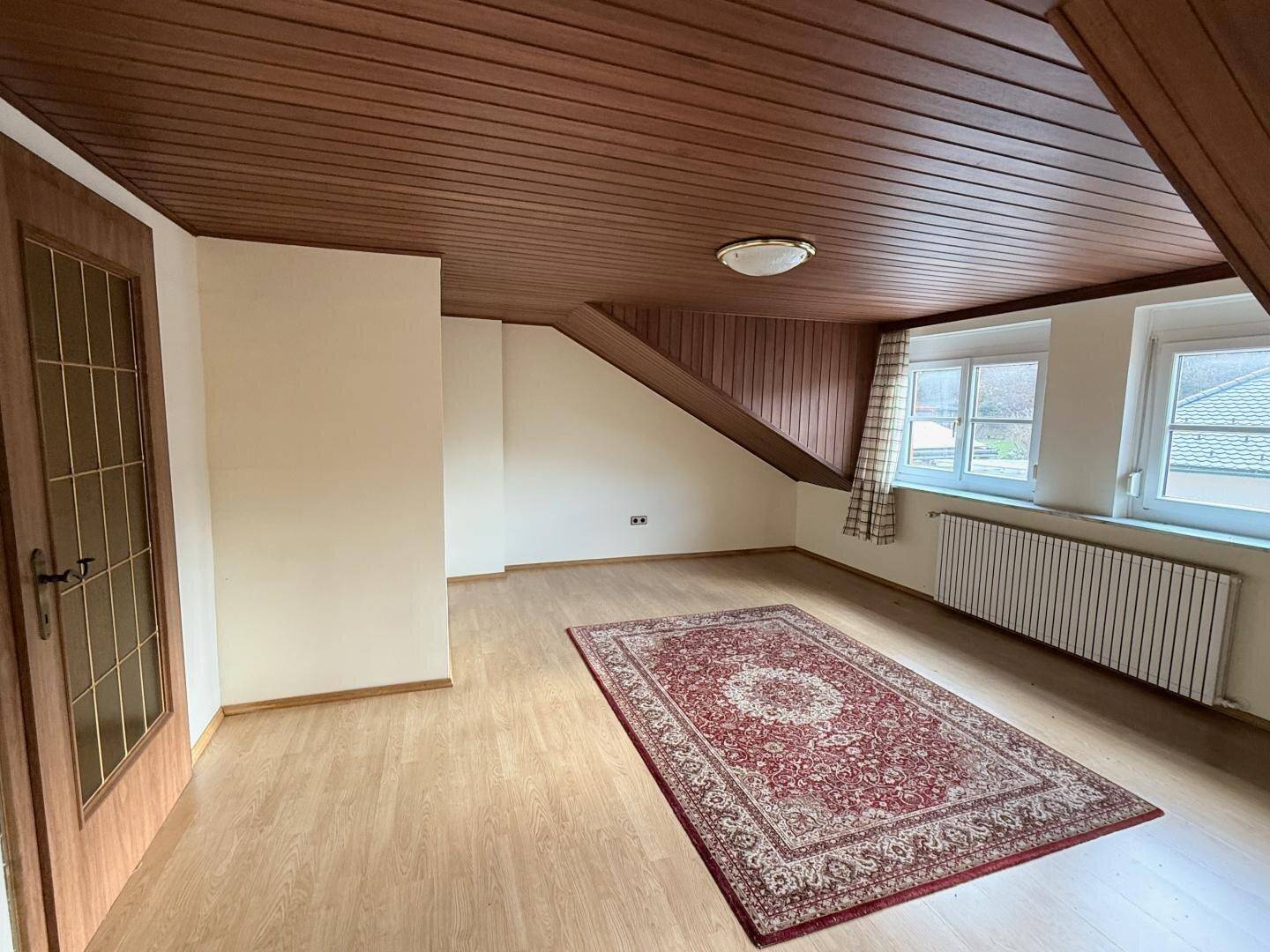 Geräumiger Raum mit Holzdachschräge, Laminatboden und Fenster.