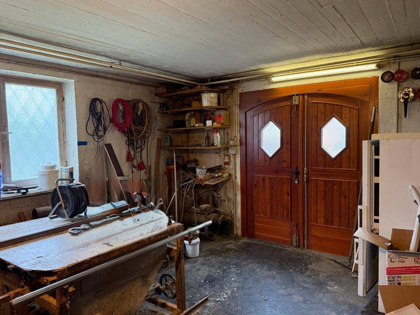 Werkstatt im Keller mit Werkbank, Regalen und Holztüren.