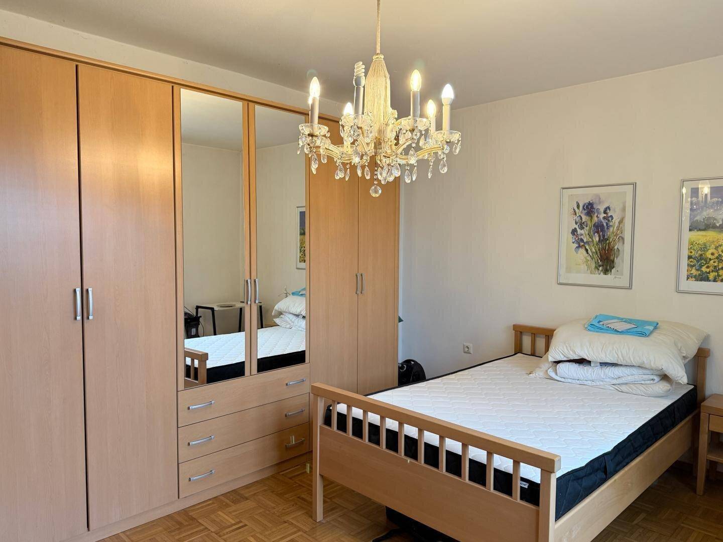 Schlafzimmer mit hellem Holzschrank, Bett und Kronleuchter.