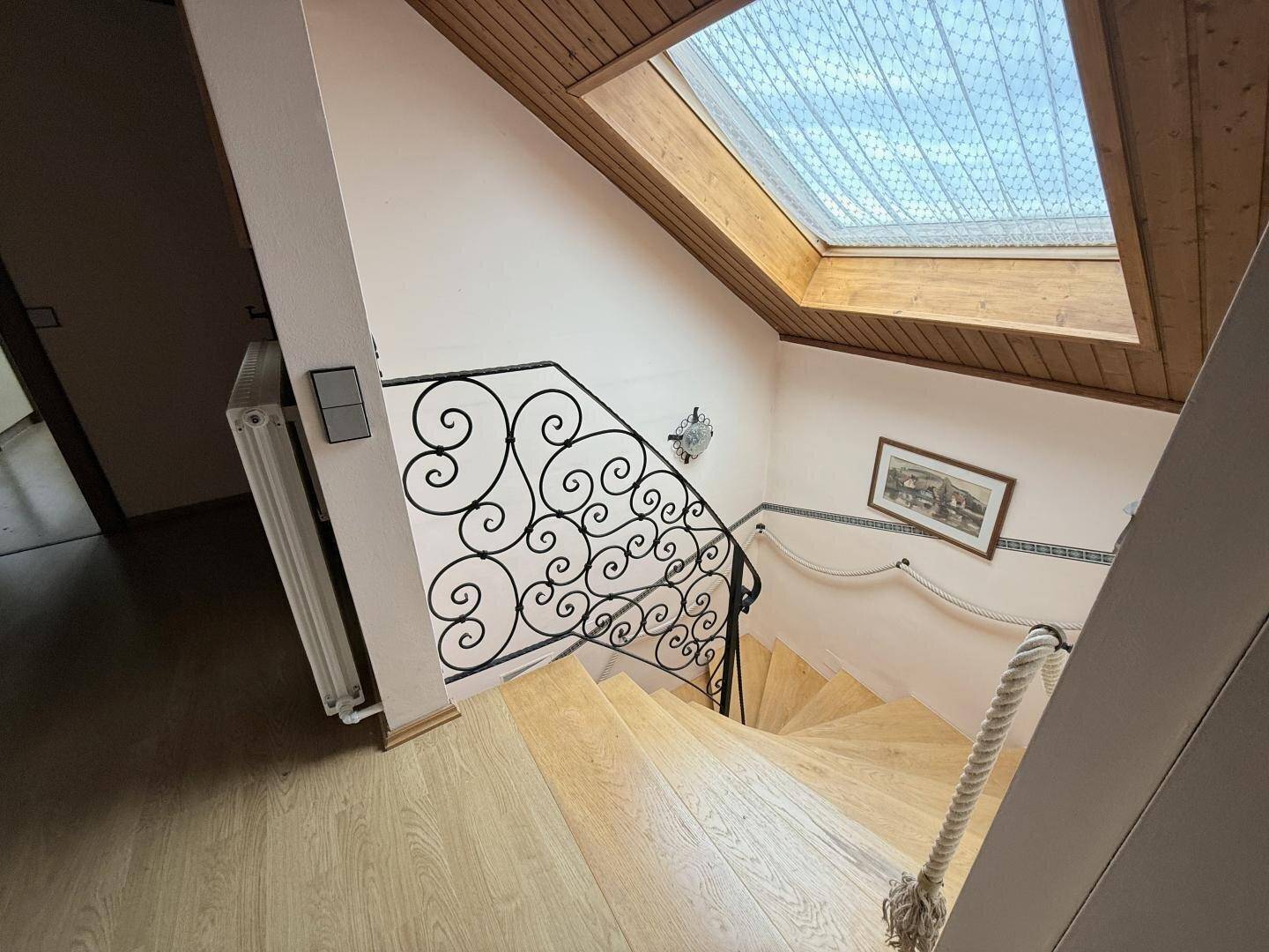 Holztreppe mit schmiedeeisernem Geländer und Dachfenster für natürliches Licht.